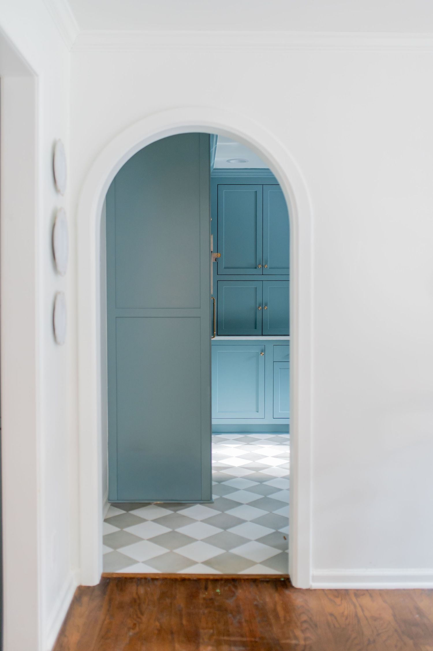 Elegant arched doorway with white trim leading to a room with blue-gray cabinetry and checkered tile floor.