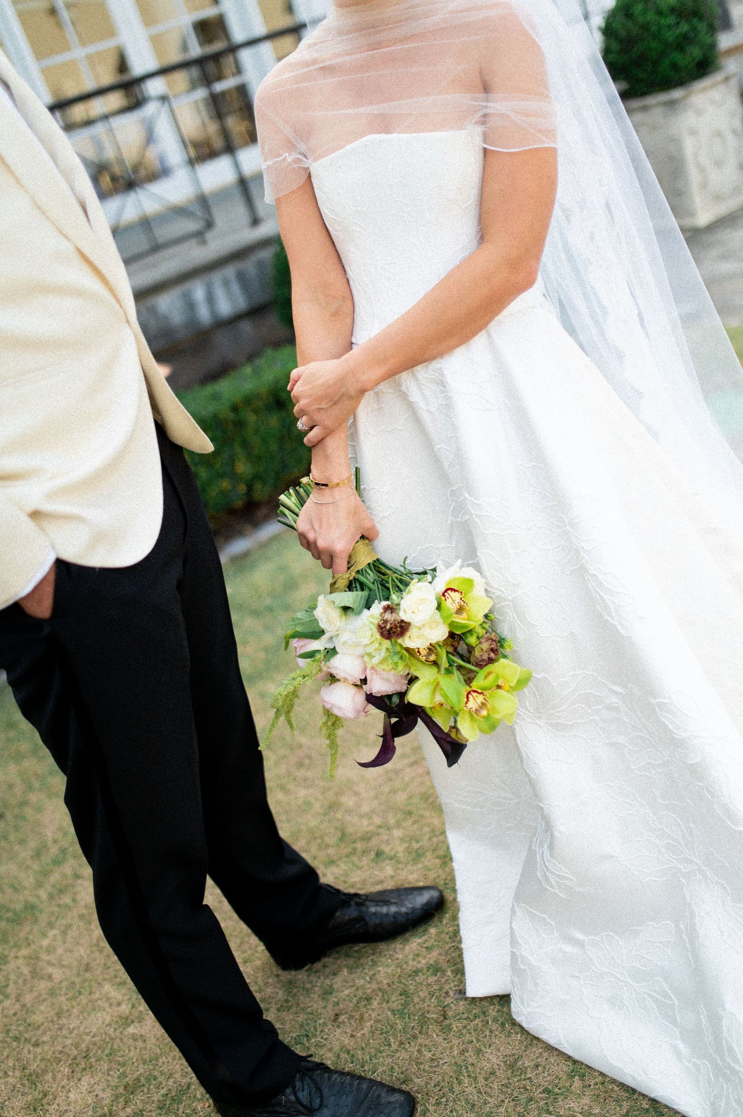 Close-up details of wedding attire and floral bouquet against formal garden setting.