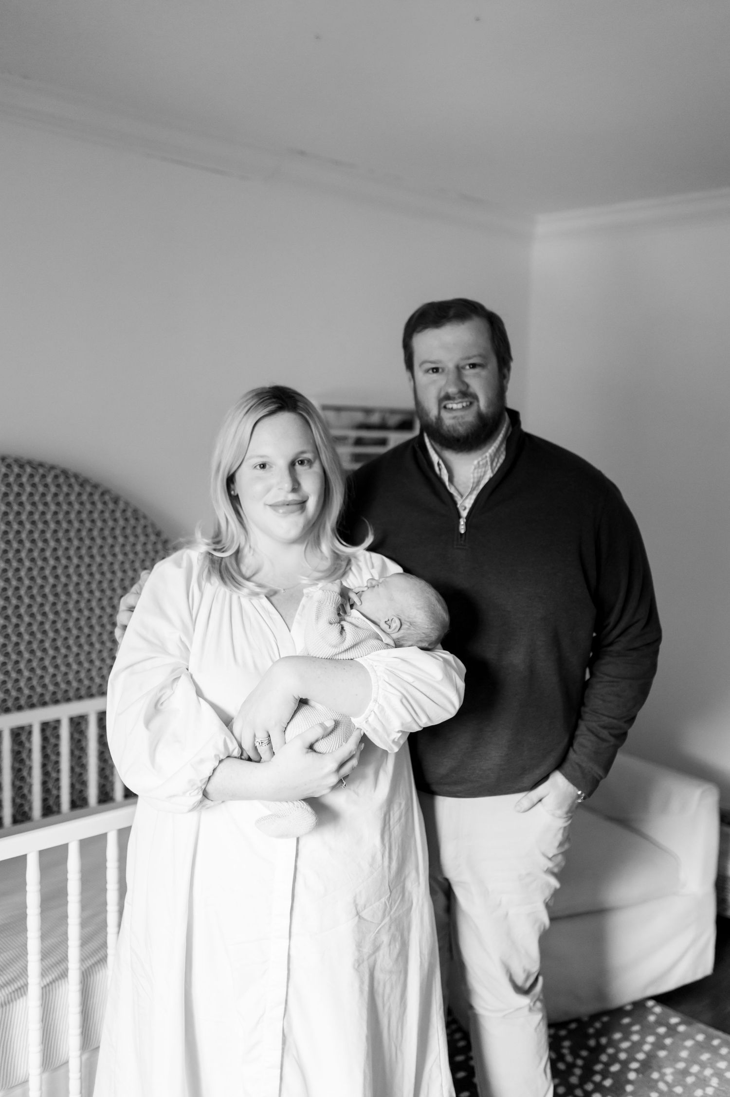 Black and white photo series showing a couple with their newborn baby in a nursery setting.