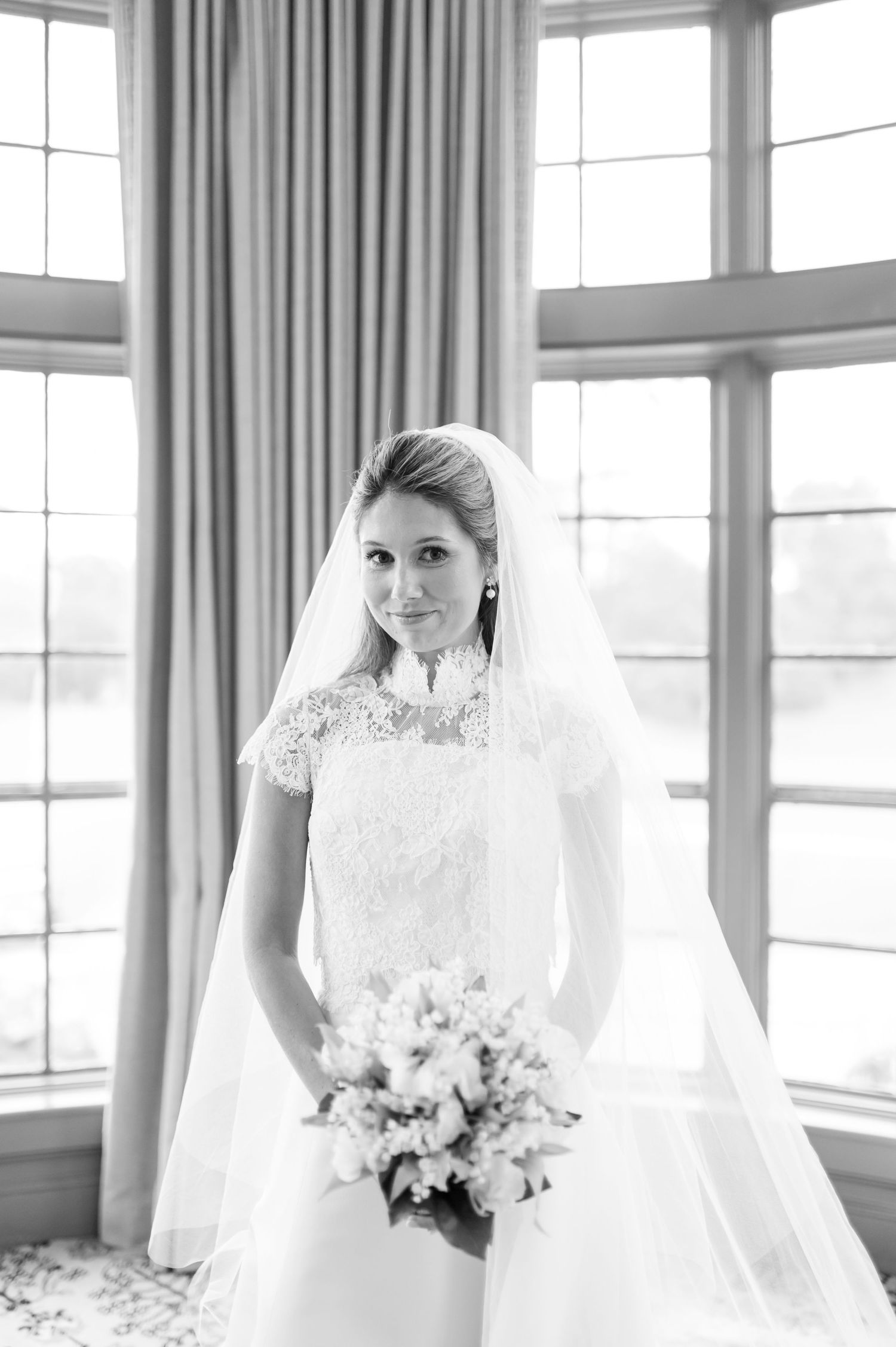 Black and white bridal portrait taken near large windows with soft natural lighting.