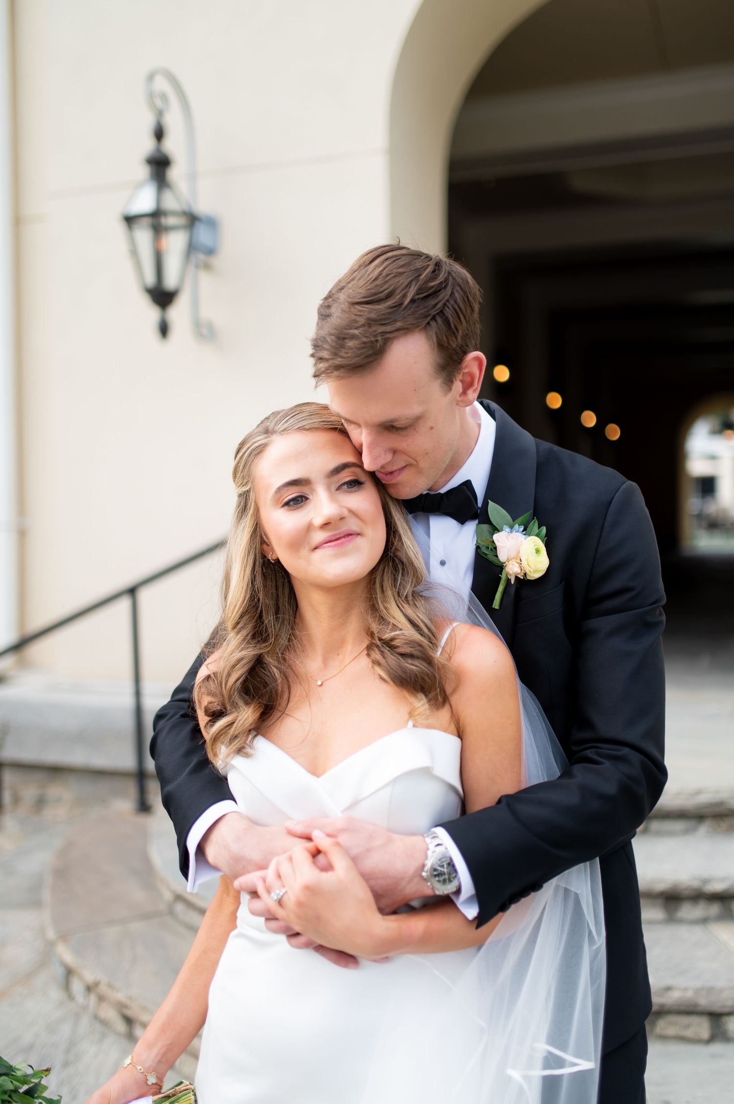 Romantic wedding couple poses together in an elegant outdoor setting with stone architecture.