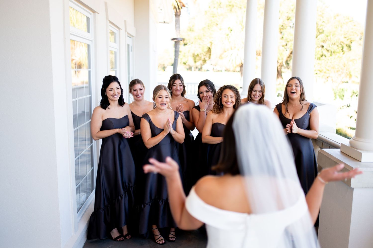 Wedding party in coordinated black dresses gathered on covered porch.