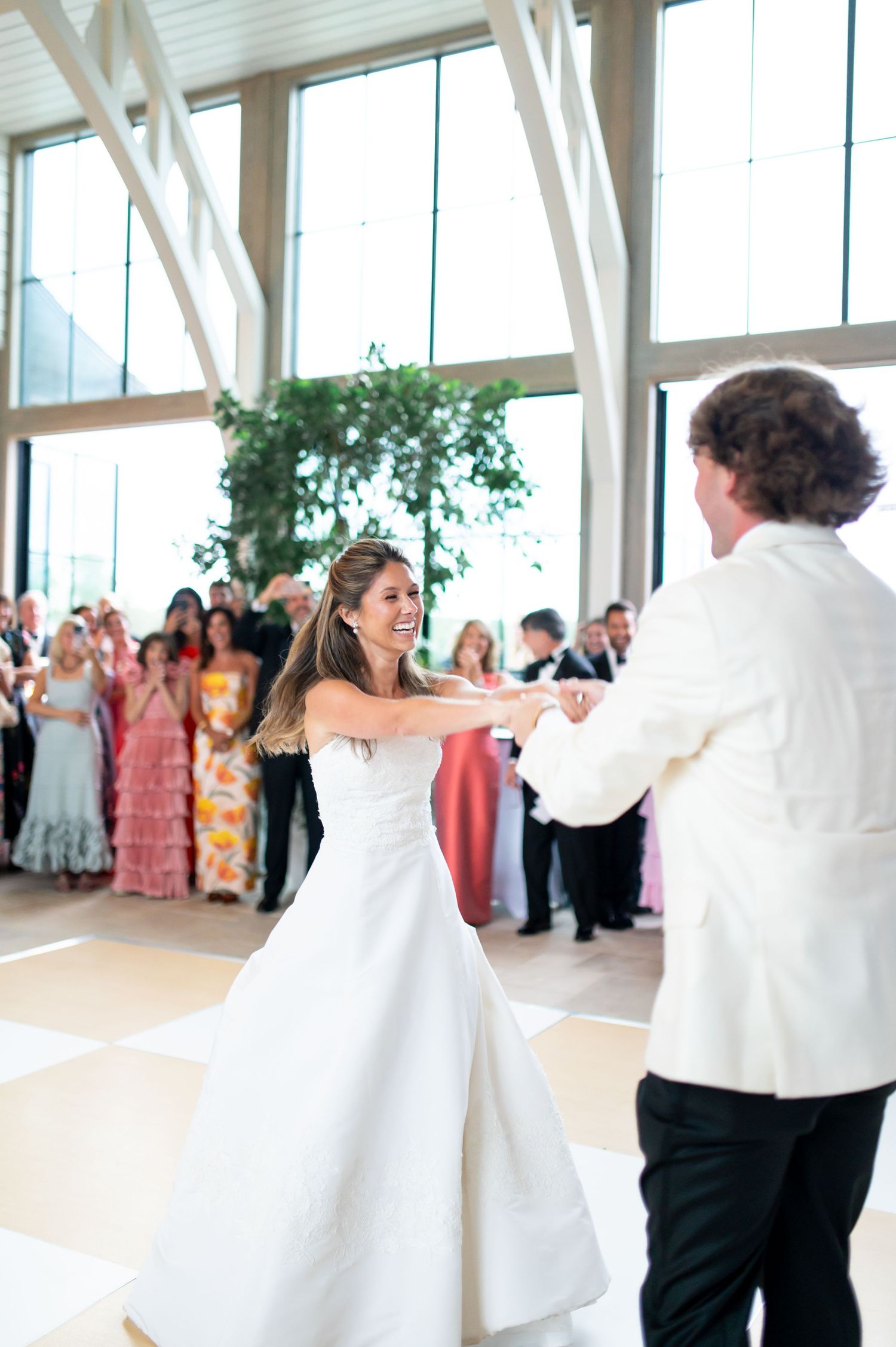 Couple performs their first dance in bright ballroom while wedding guests look on.