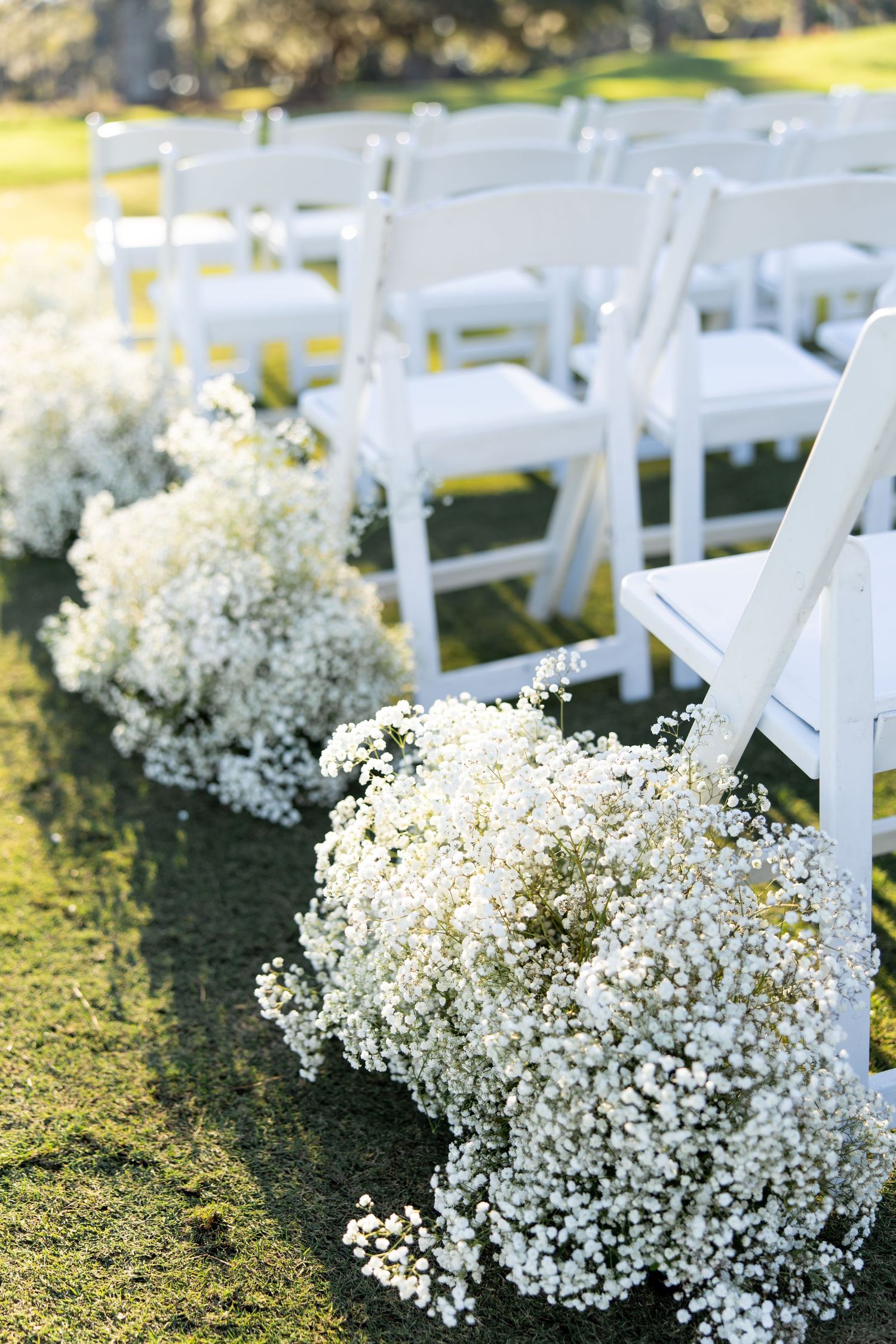 White baby's breath flowers line the aisle of an outdoor wedding ceremony with white folding chairs.