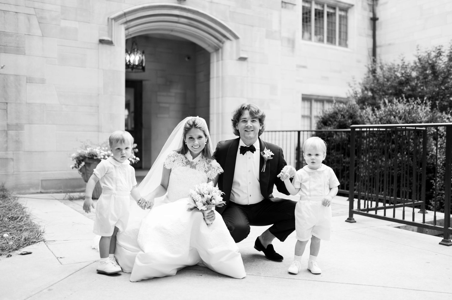 Wedding party relaxing on stone steps of historic building in formal attire.