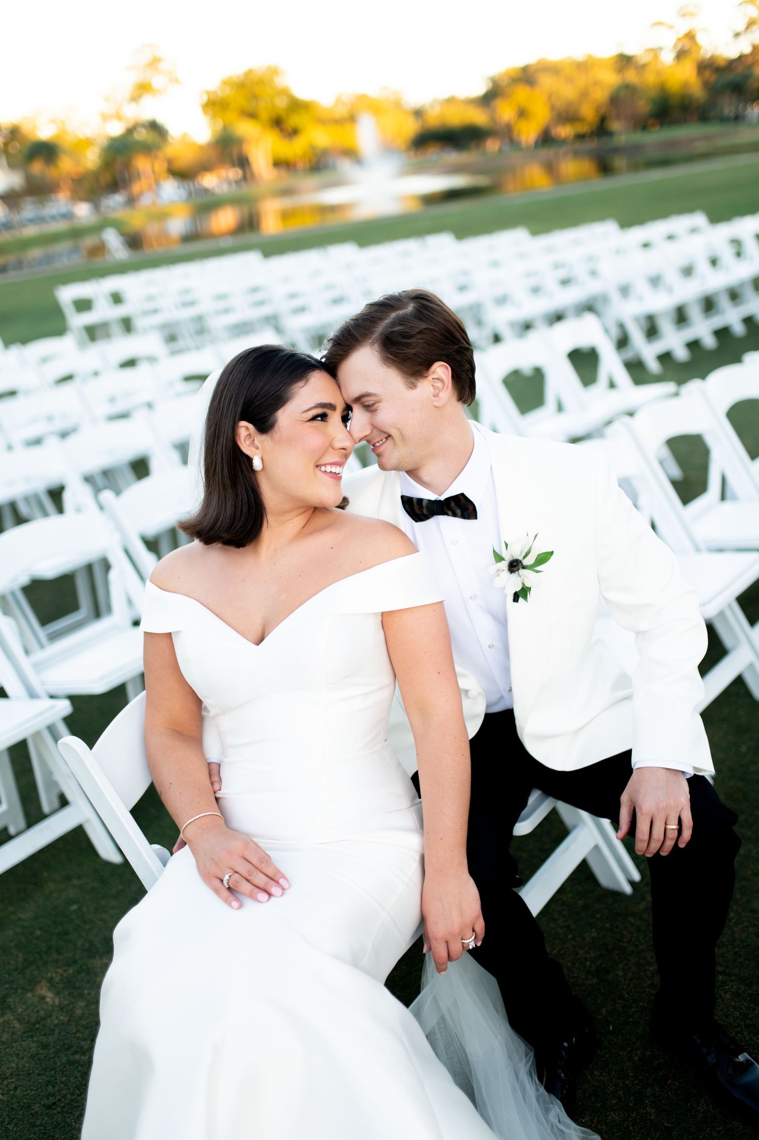 Wedding couple posing among white ceremony chairs outdoors during golden hour.