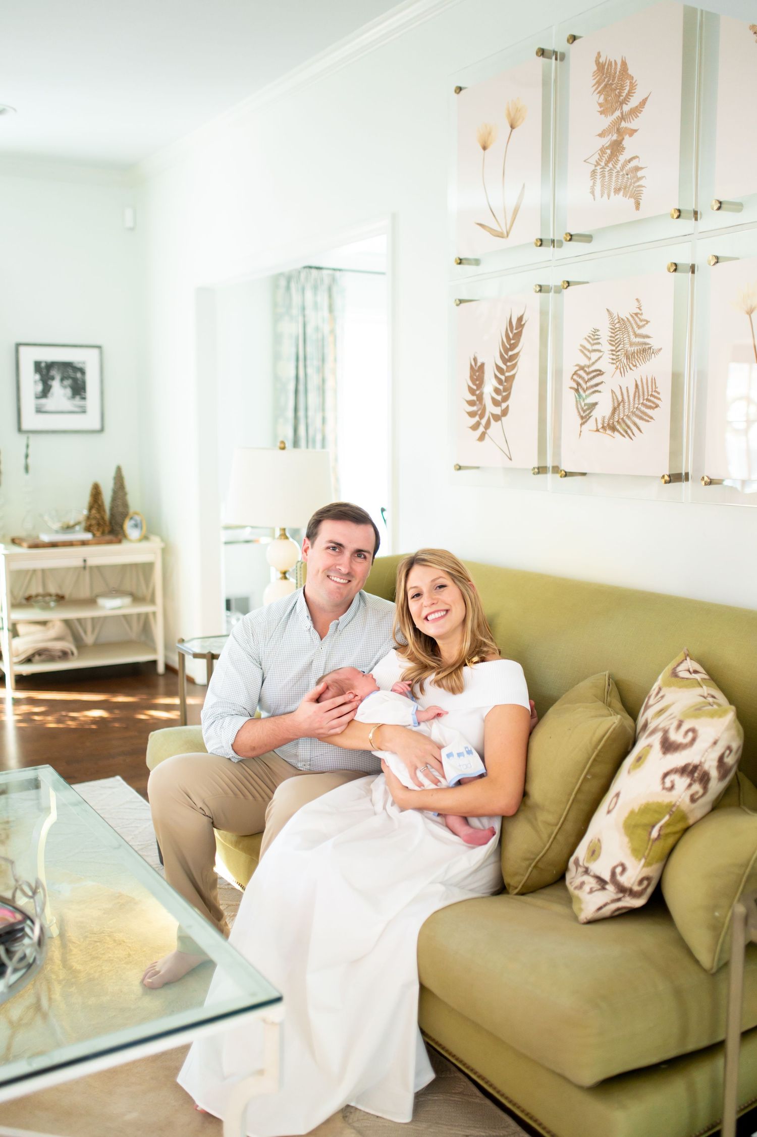 Newlyweds relax on olive green couch with their pet in bright modern living room.