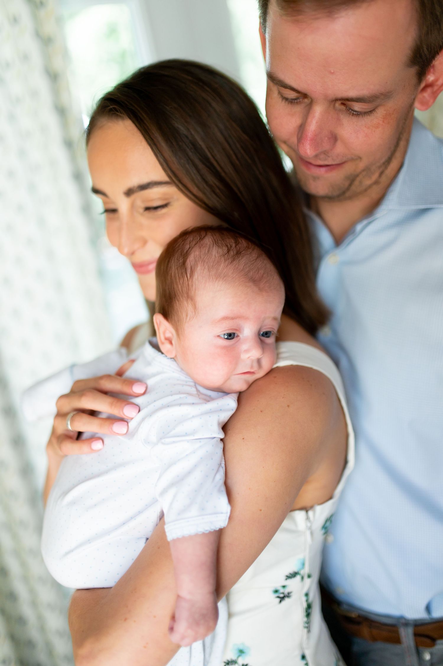 Intimate family moments captured as parents cradle their newborn baby in a sunlit room.
