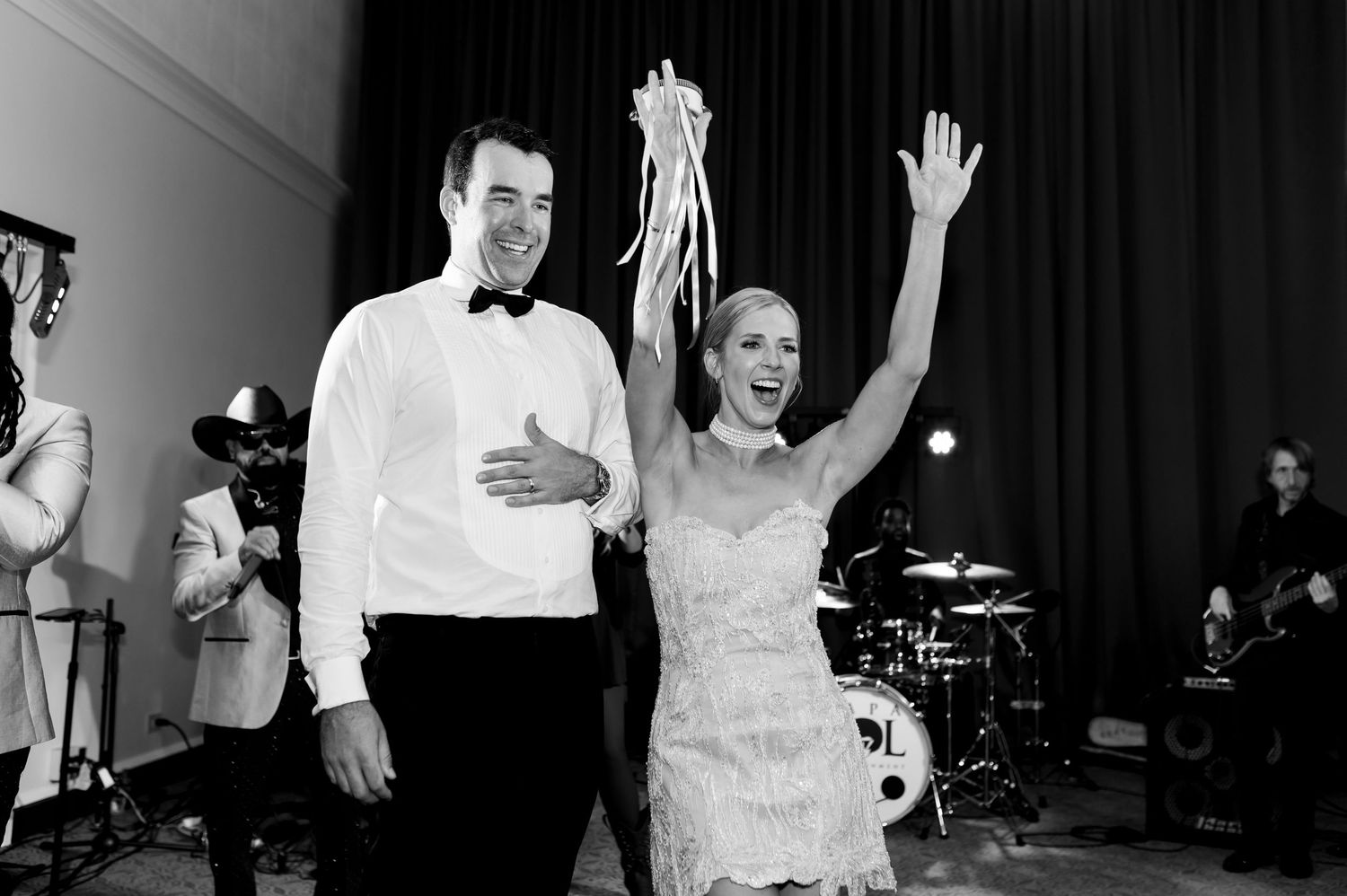 Black and white photo of wedding guests dancing at reception with dramatic lighting.