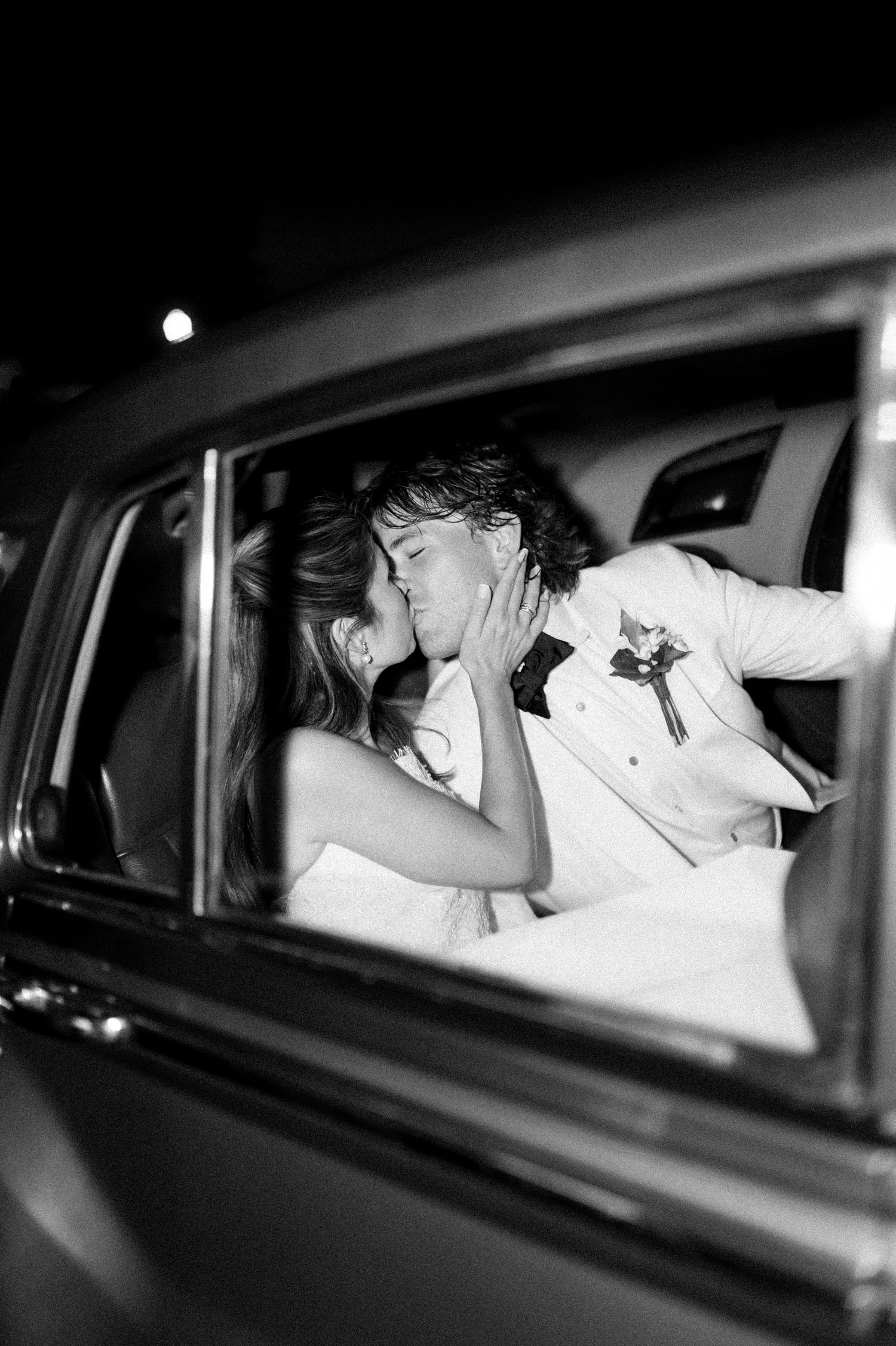 Black and white photo of newlyweds sharing an intimate moment in the back of a car.