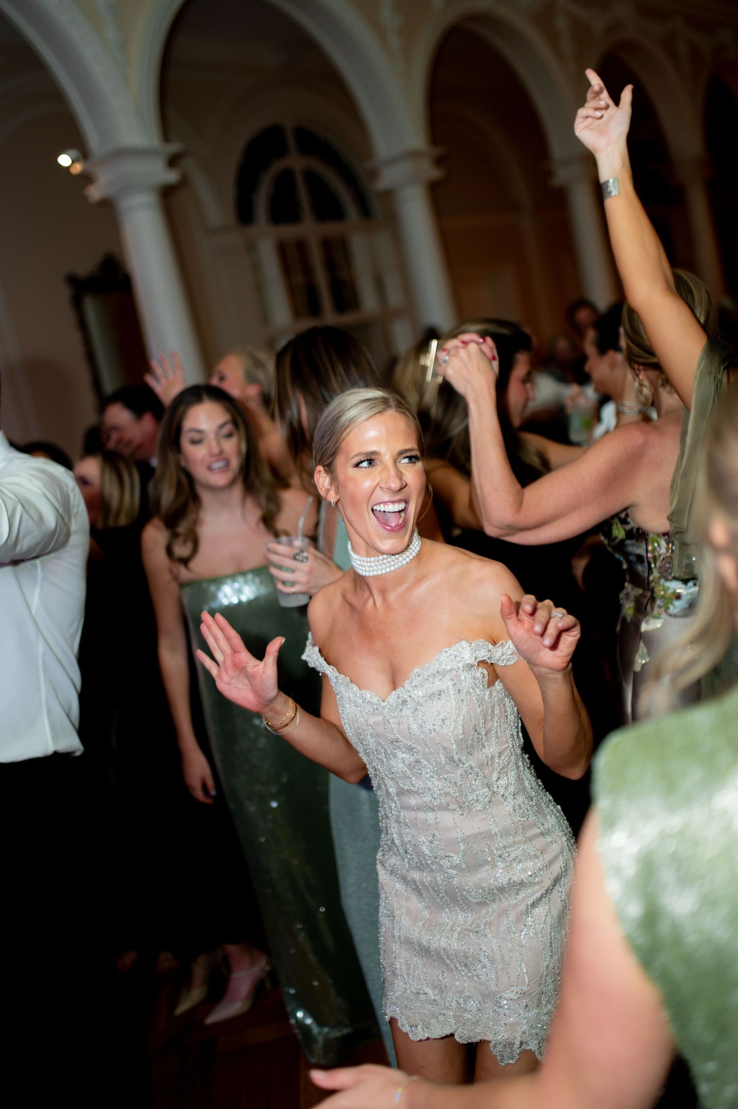 Lively dance floor celebration at an elegant wedding reception with chandeliers.