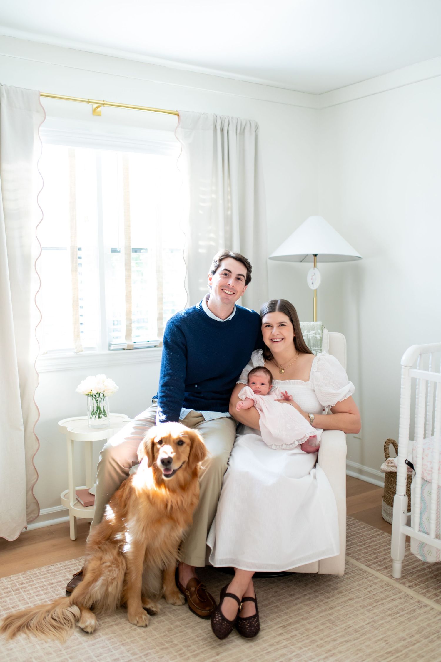 A golden retriever dog sits with a family in a bright white room with windows and curtains.