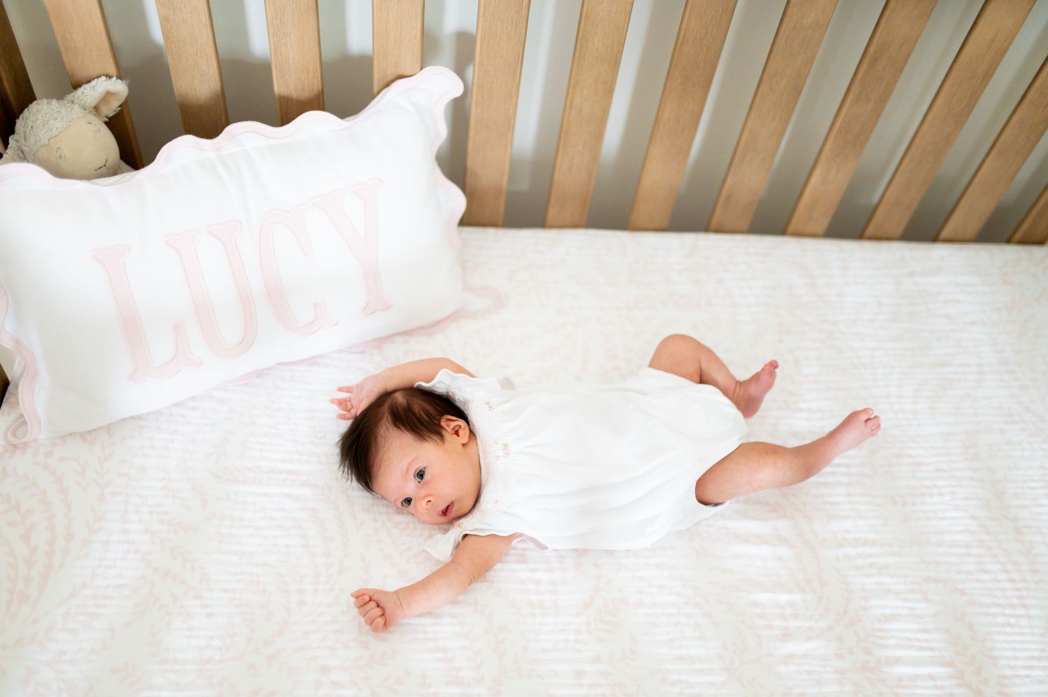 A sleeping baby lies peacefully in a wooden crib with white bedding.