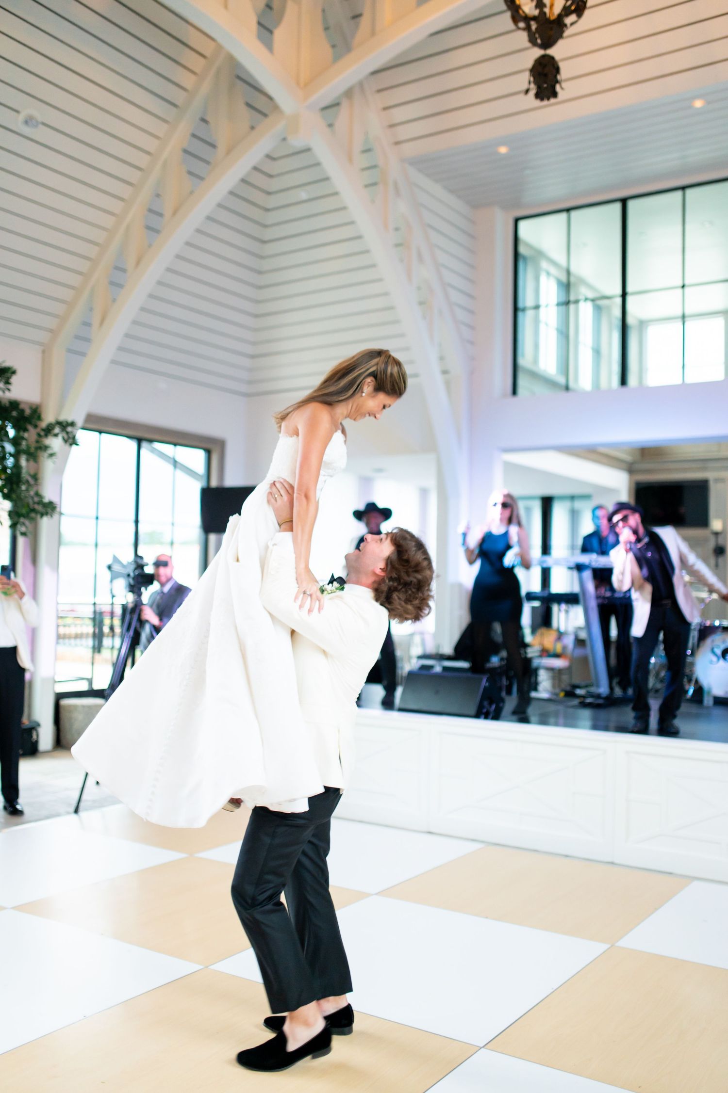 A joyful lift during a wedding dance on a checkered floor in an elegant venue.