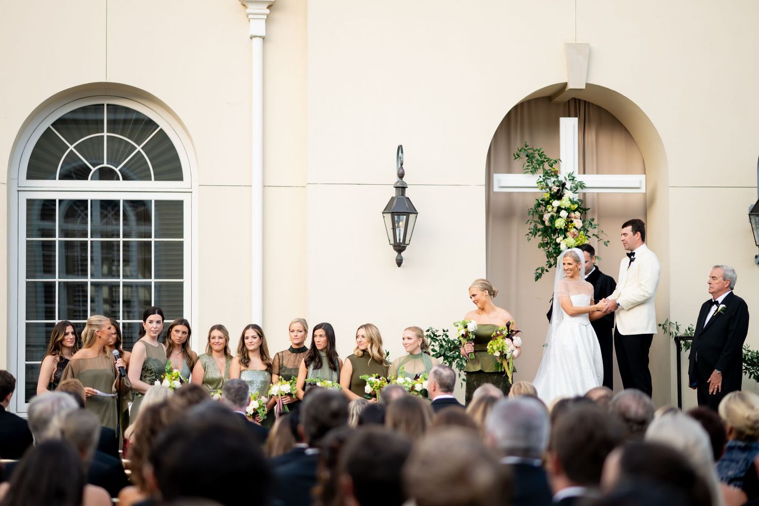 Large crowd of wedding attendees standing in front of a classical building facade.