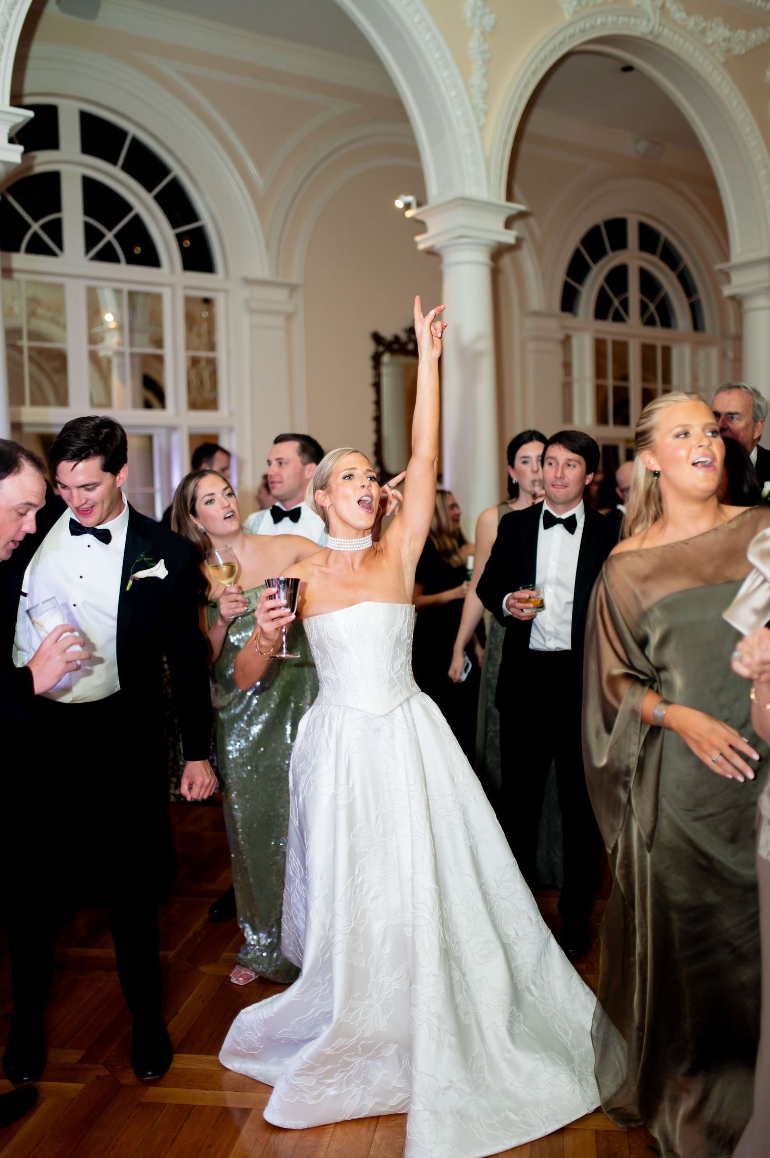 Wedding guests celebrate with the couple during a lively reception in an ornate ballroom.