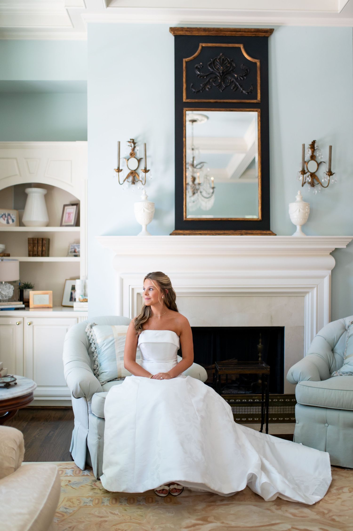 A white wedding dress elegantly displayed in a formal living room with blue accents and a fireplace.