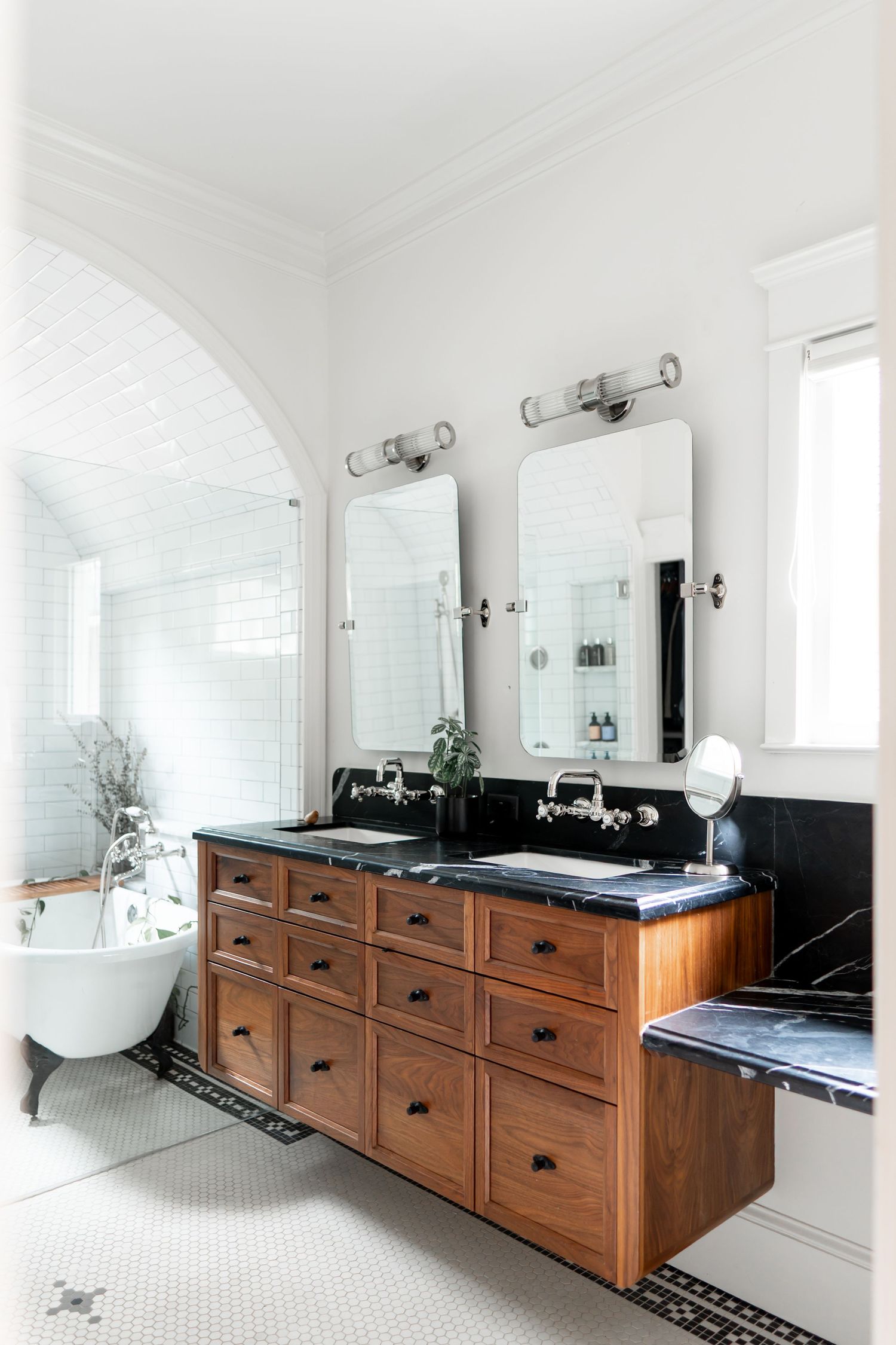 Modern bathroom interior with dark wood cabinets, black countertops, and a freestanding tub under arched ceiling.