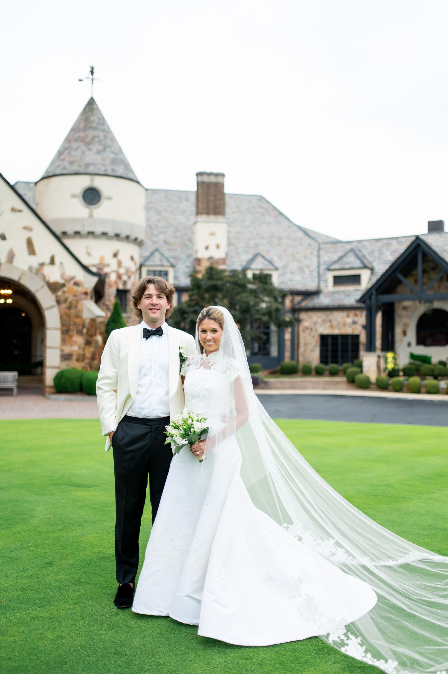 Formal wedding portrait on lawn with stone church backdrop and flowing cathedral veil.