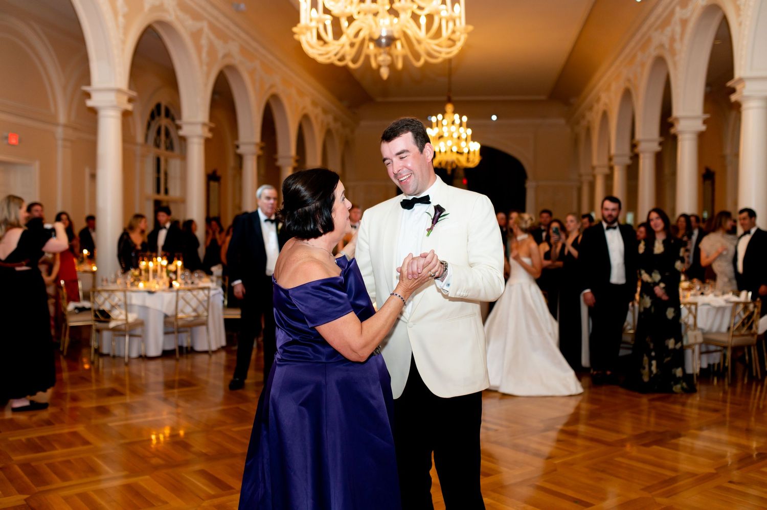 Wedding celebration with dancing couples in an ornate ballroom with warm lighting.