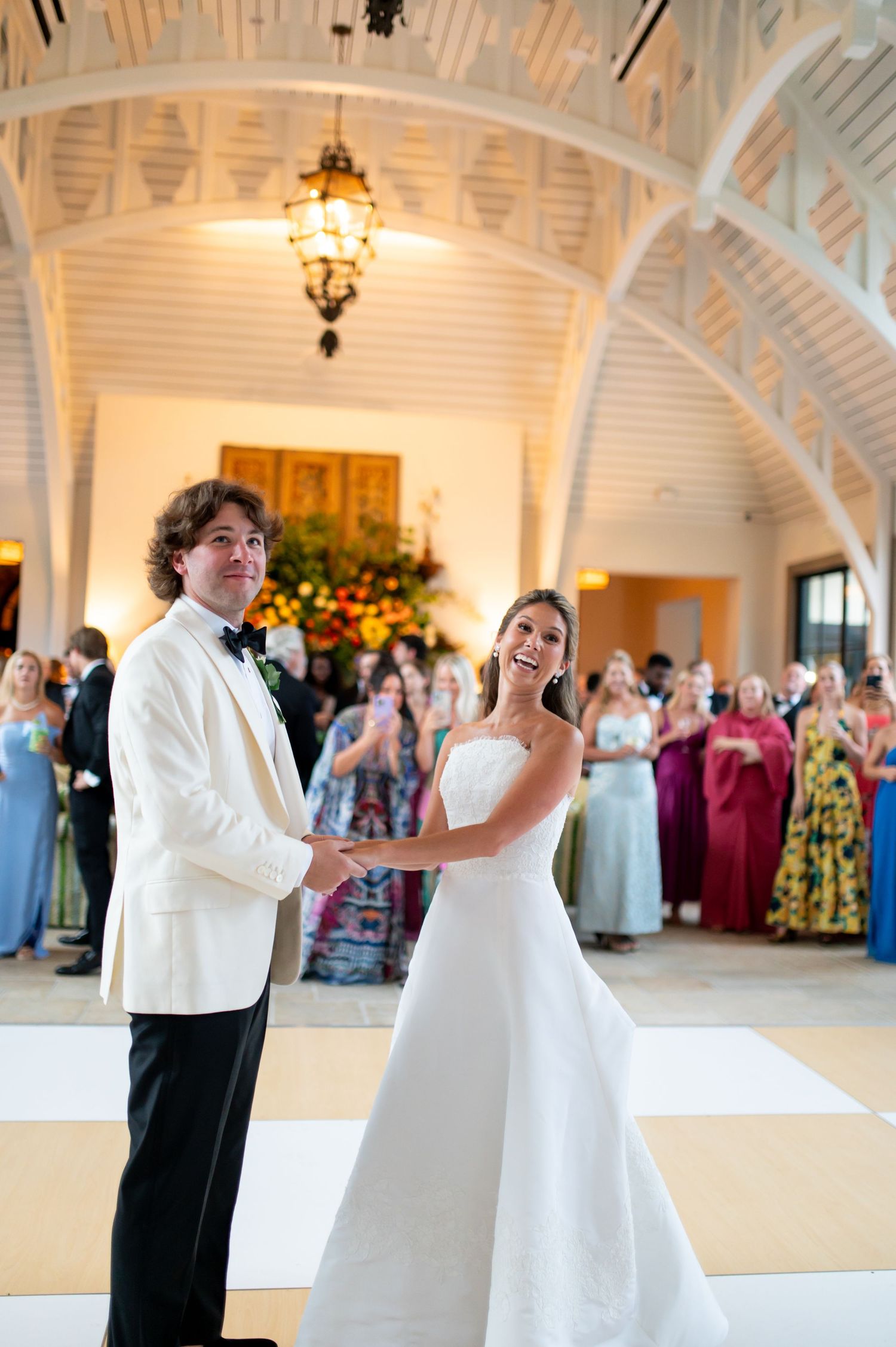Newlyweds share their first dance in an elegant white-arched ballroom with chandelier.