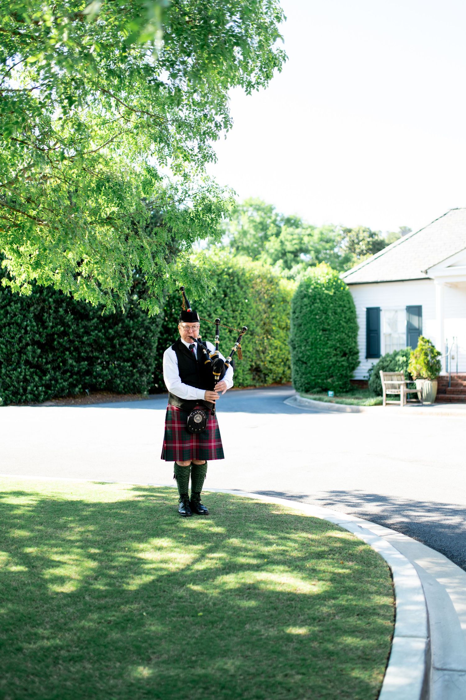 Scottish bagpiper in traditional tartan kilt performing on manicured lawn at wedding venue.