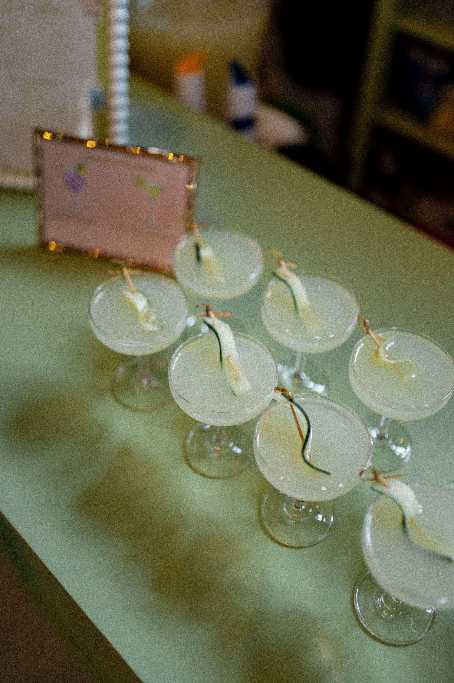 Elegant coupe glasses filled with white cocktails garnished with ribbon on a green table.