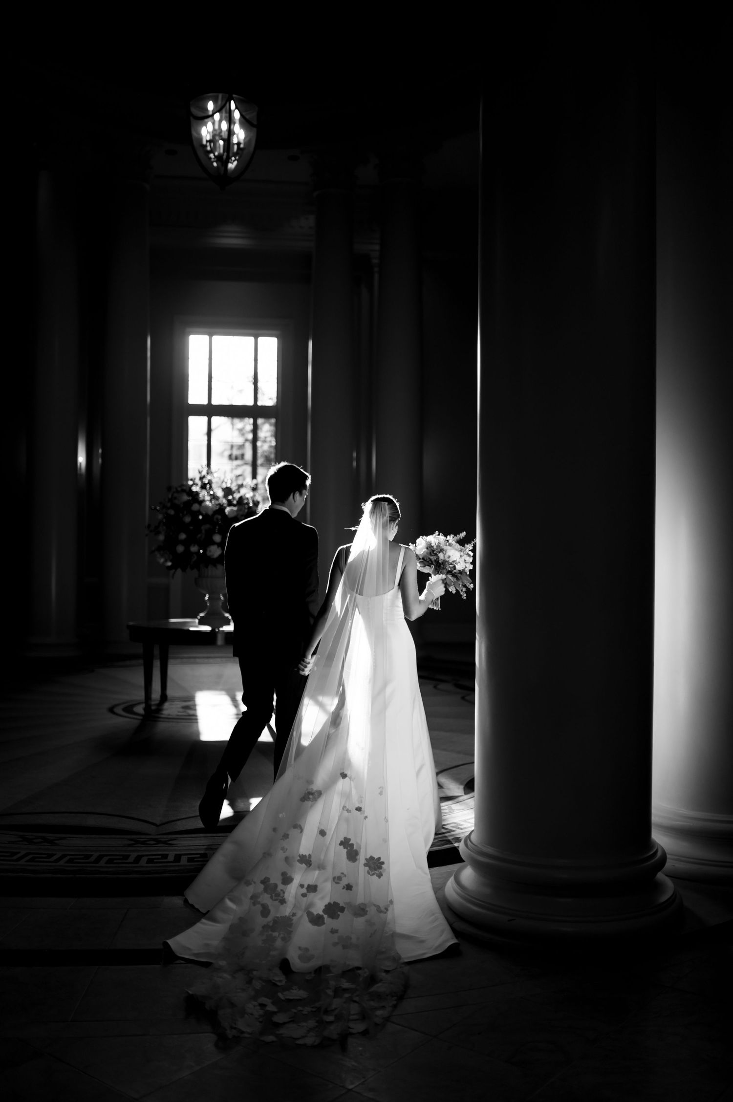 Dramatic black and white wedding photos in a columned hallway with natural window light.