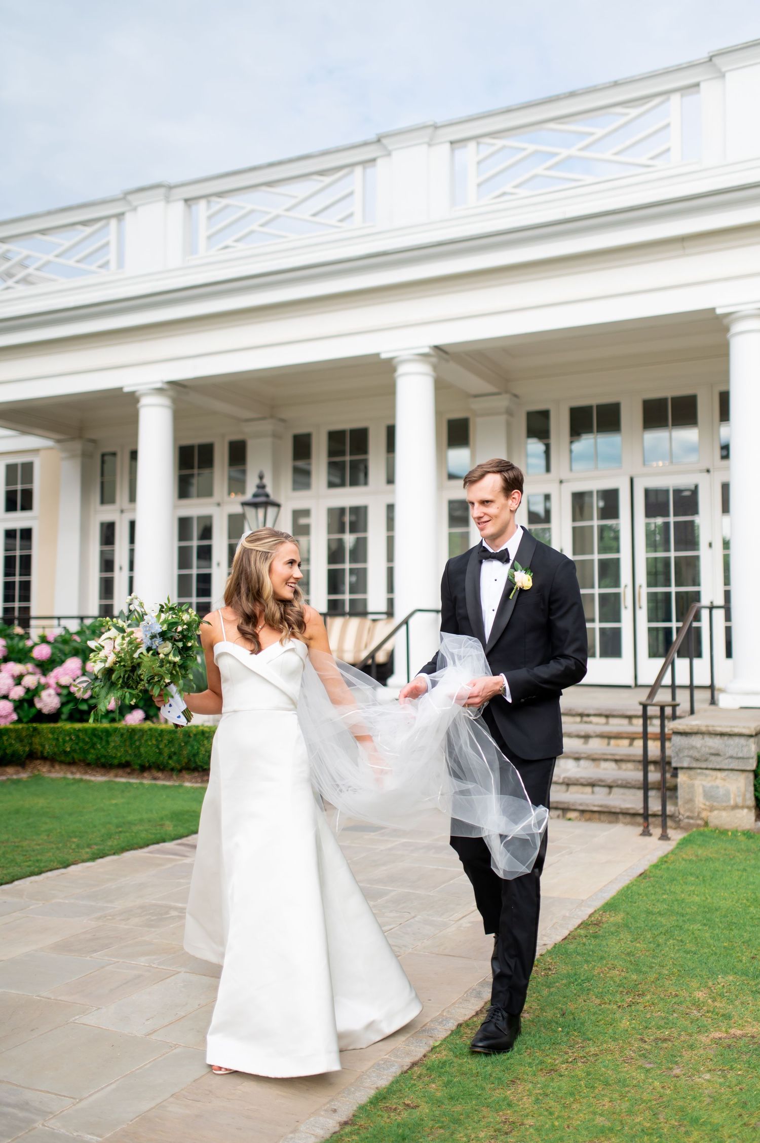 Wedding couple dances and twirls on a manicured lawn in front of a white columned building.