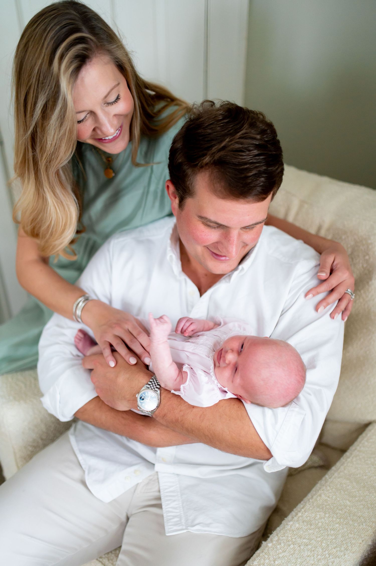 Family bonding moment on a cream colored couch as they lovingly hold and gaze at their newborn baby.
