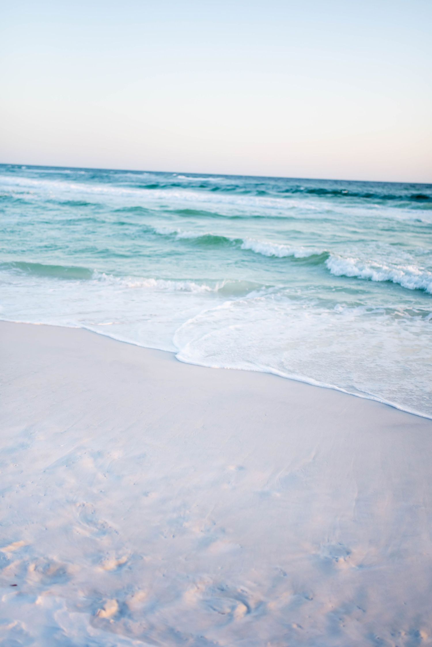 Serene beach scene with gentle waves rolling onto white sand at sunset.