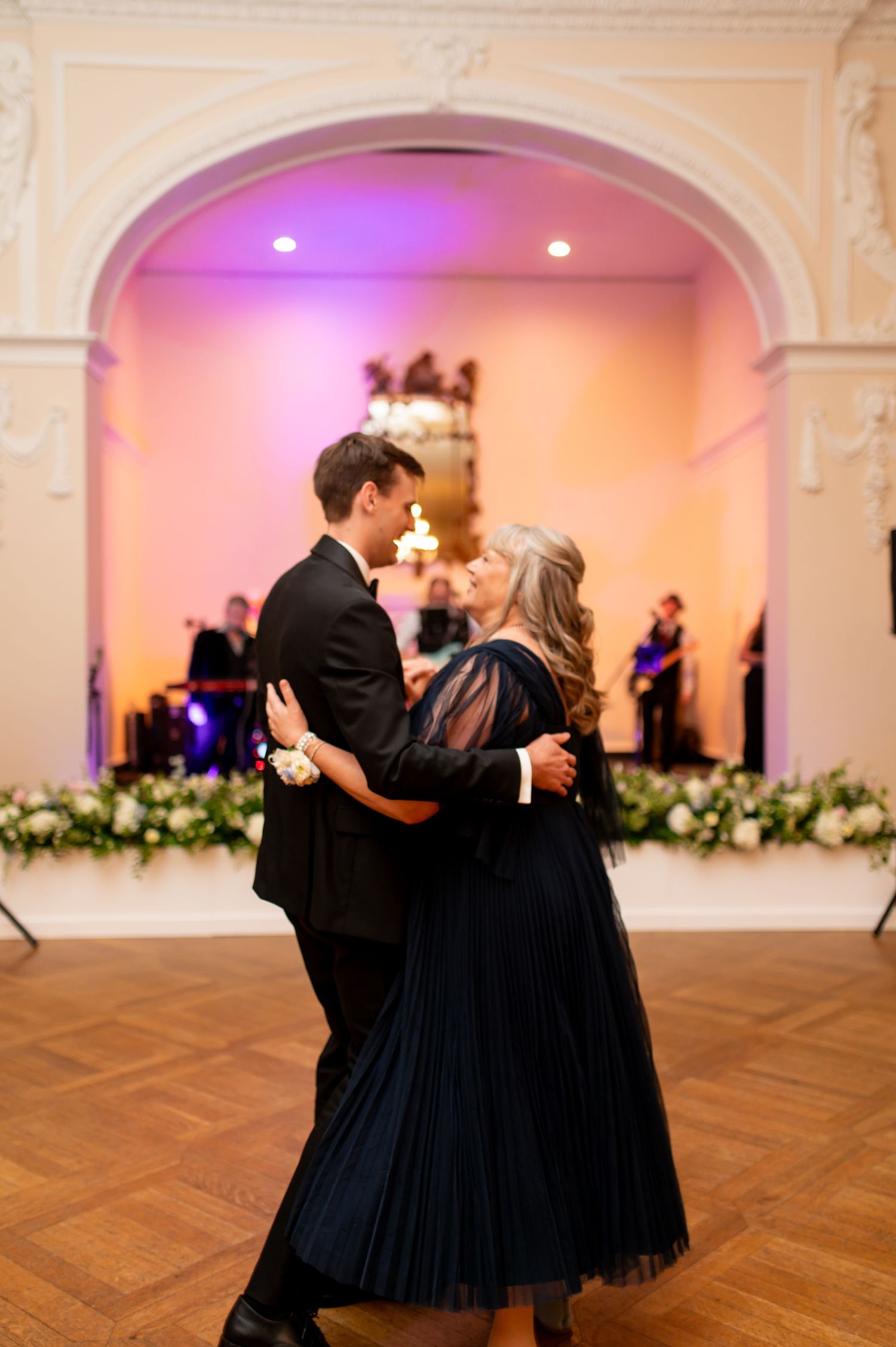 Formal dance in a ballroom with pink mood lighting and ornate architectural details.