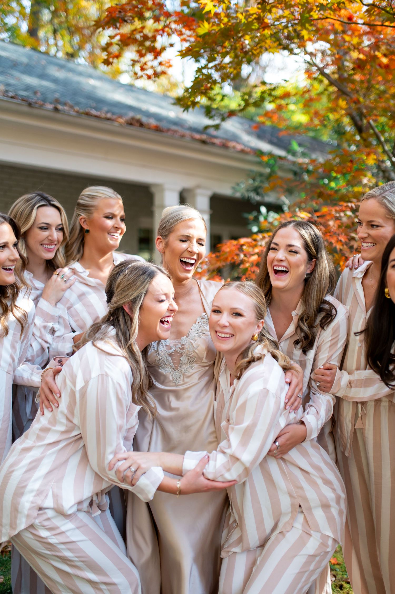 Group wearing matching silk robes sharing joyful laughter during autumn wedding preparations.