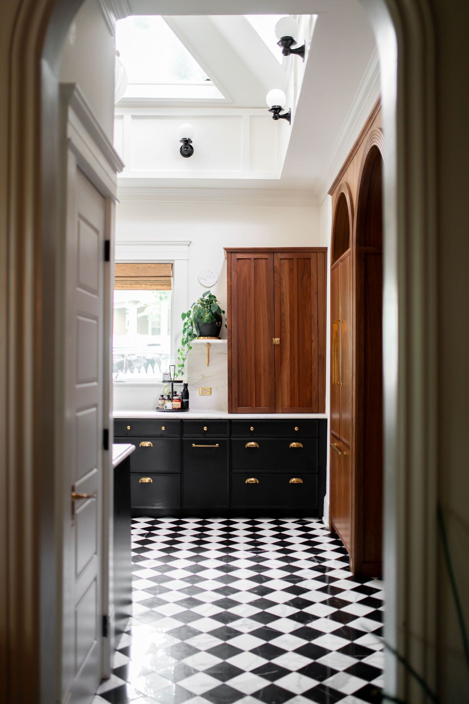 Modern hallway with dramatic black and white checkered floor and rich wood cabinets under skylights.