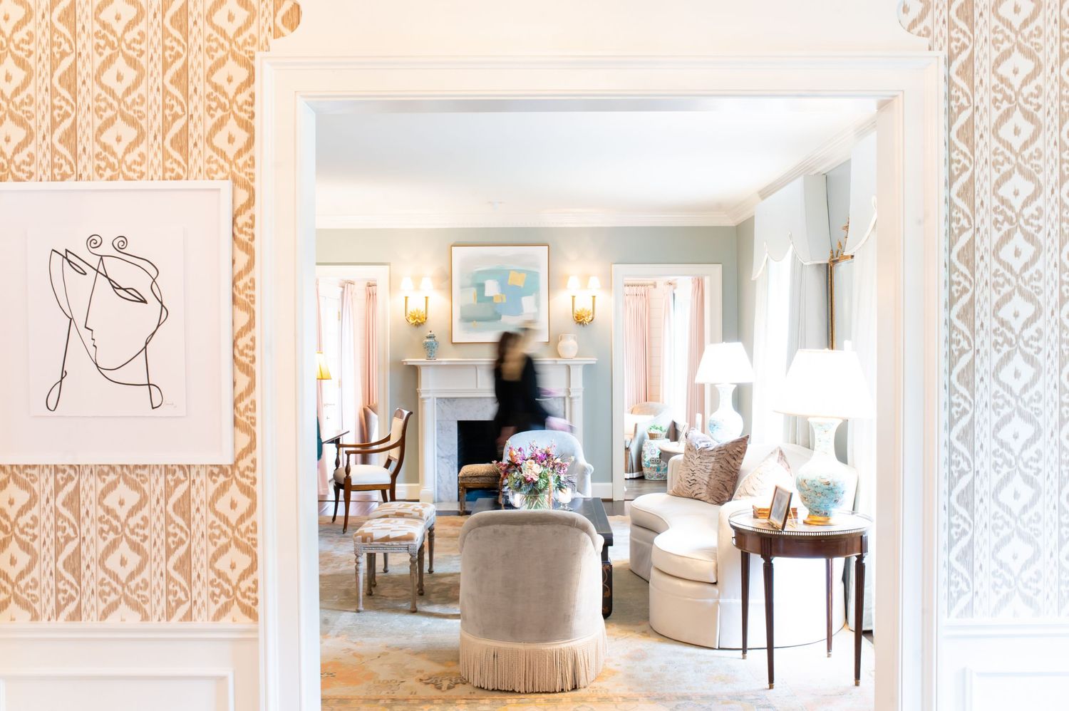 Elegant living room with pastel decor, fireplace, fringe chairs, and orange ikat wallpaper in a classic interior design.