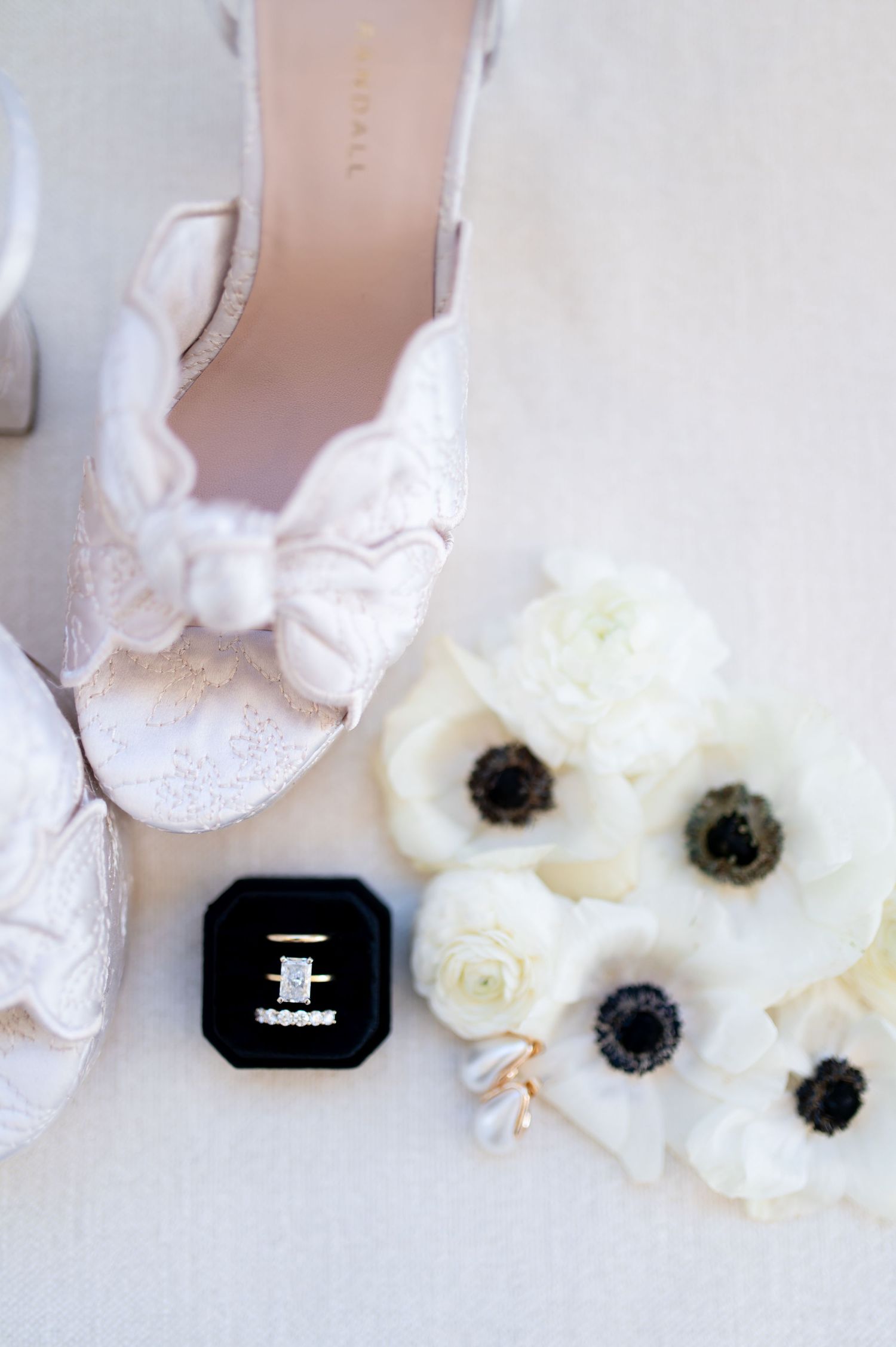 White anemone flowers arranged beside black ring box on light surface.