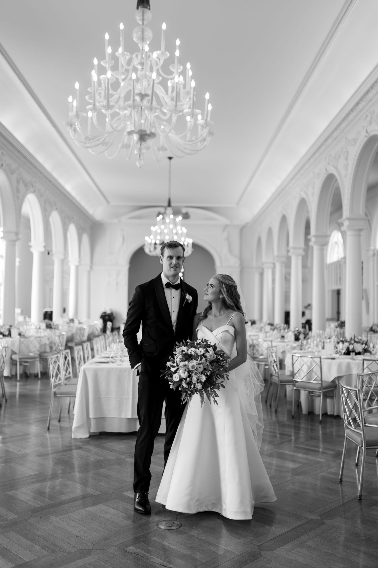Elegant ballroom with crystal chandeliers and white decor set for a wedding reception.