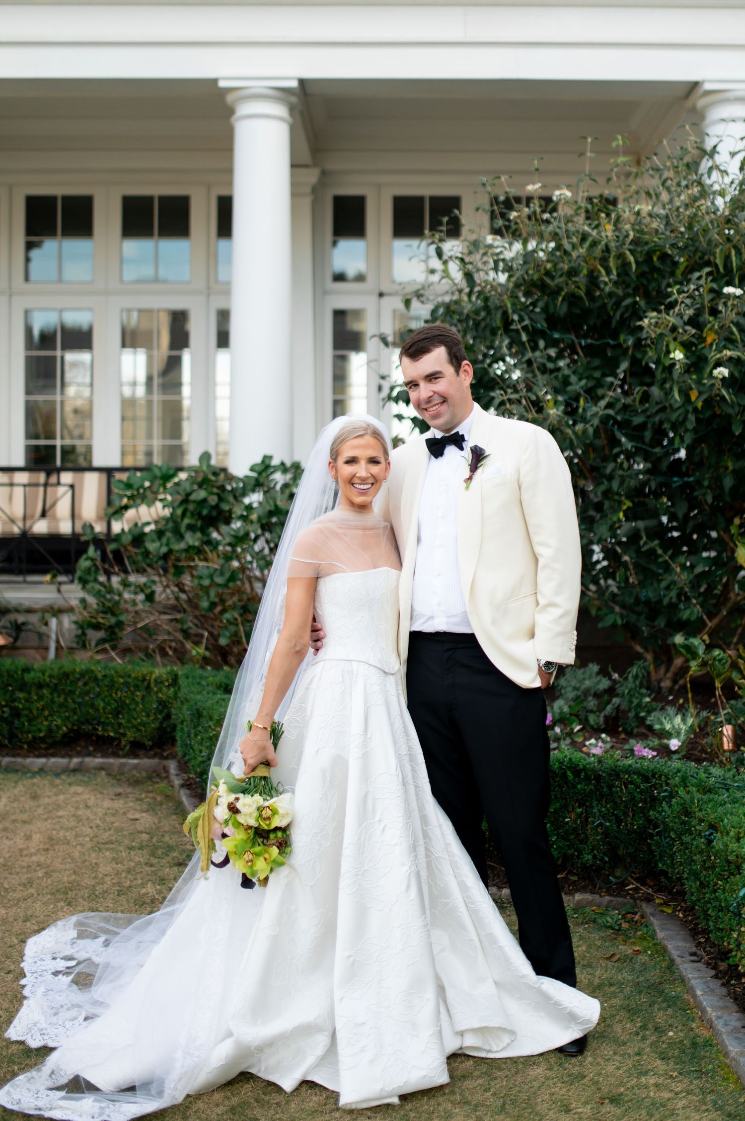 Wedding photography session in front of a classic white columned building with landscaped gardens.