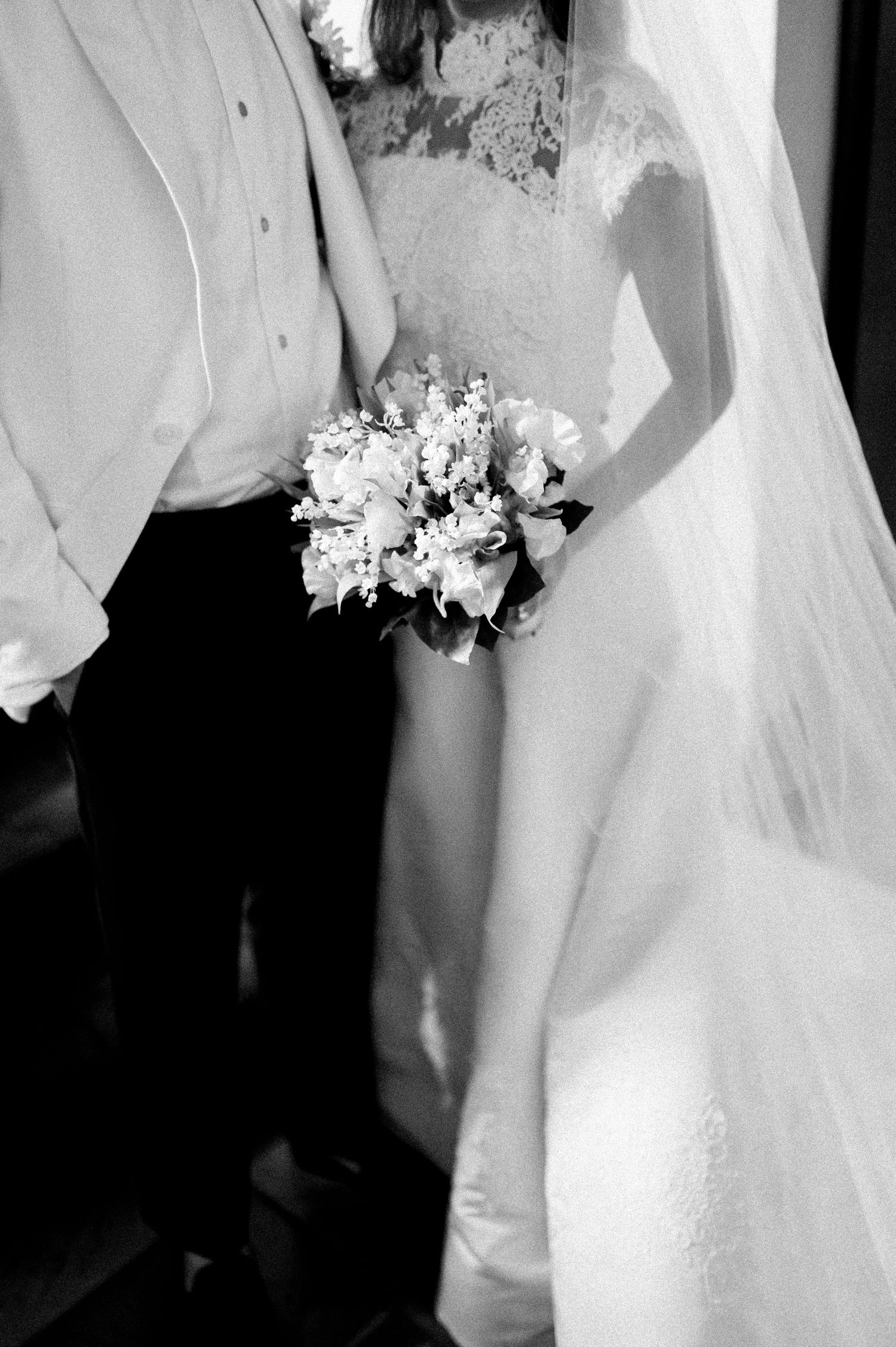 Close-up details of a bride's white lace wedding dress and floral bouquet in black and white.