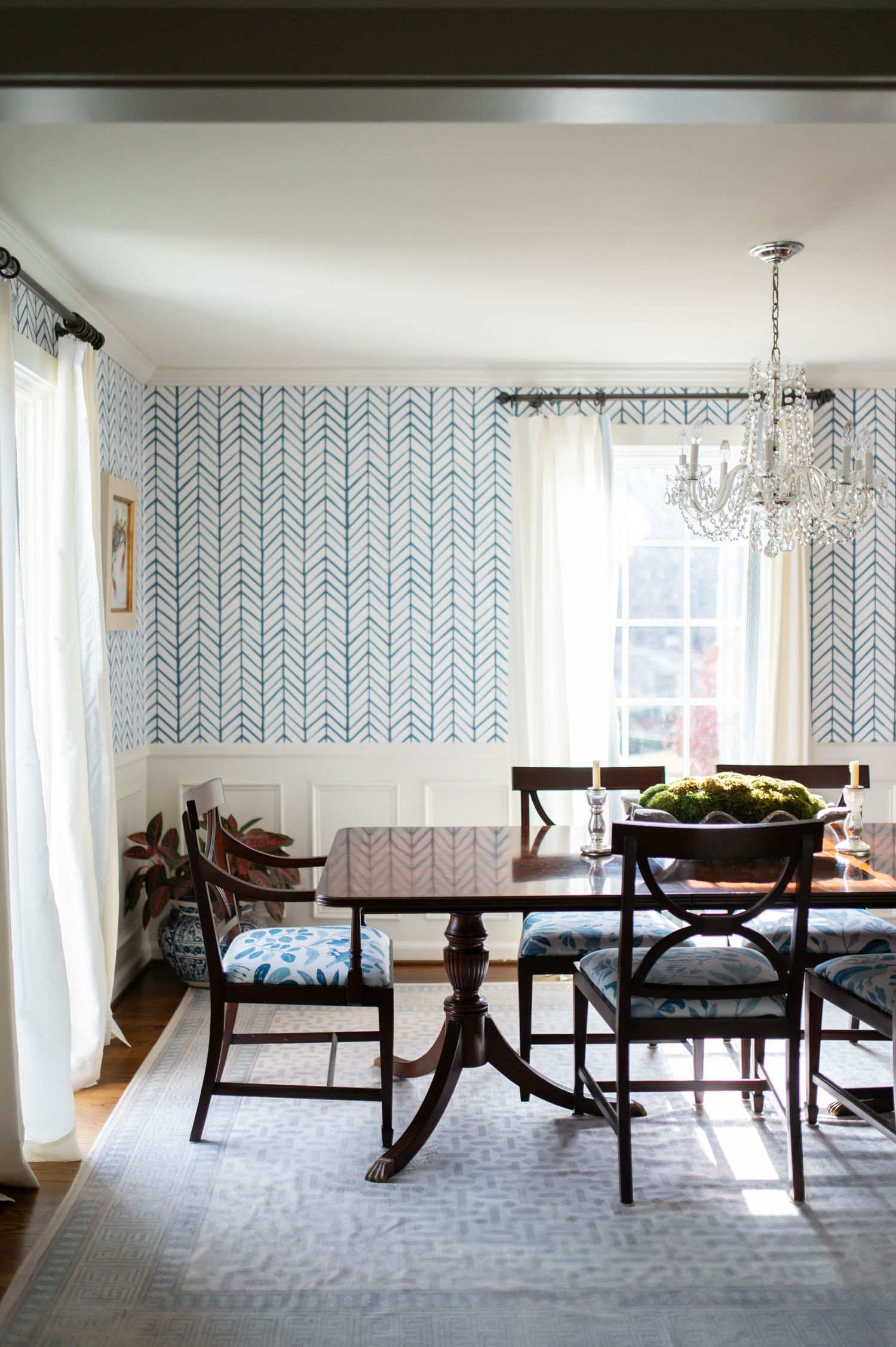 Modern dining room with blue and white herringbone wallpaper, dark wood furniture, and a crystal chandelier.