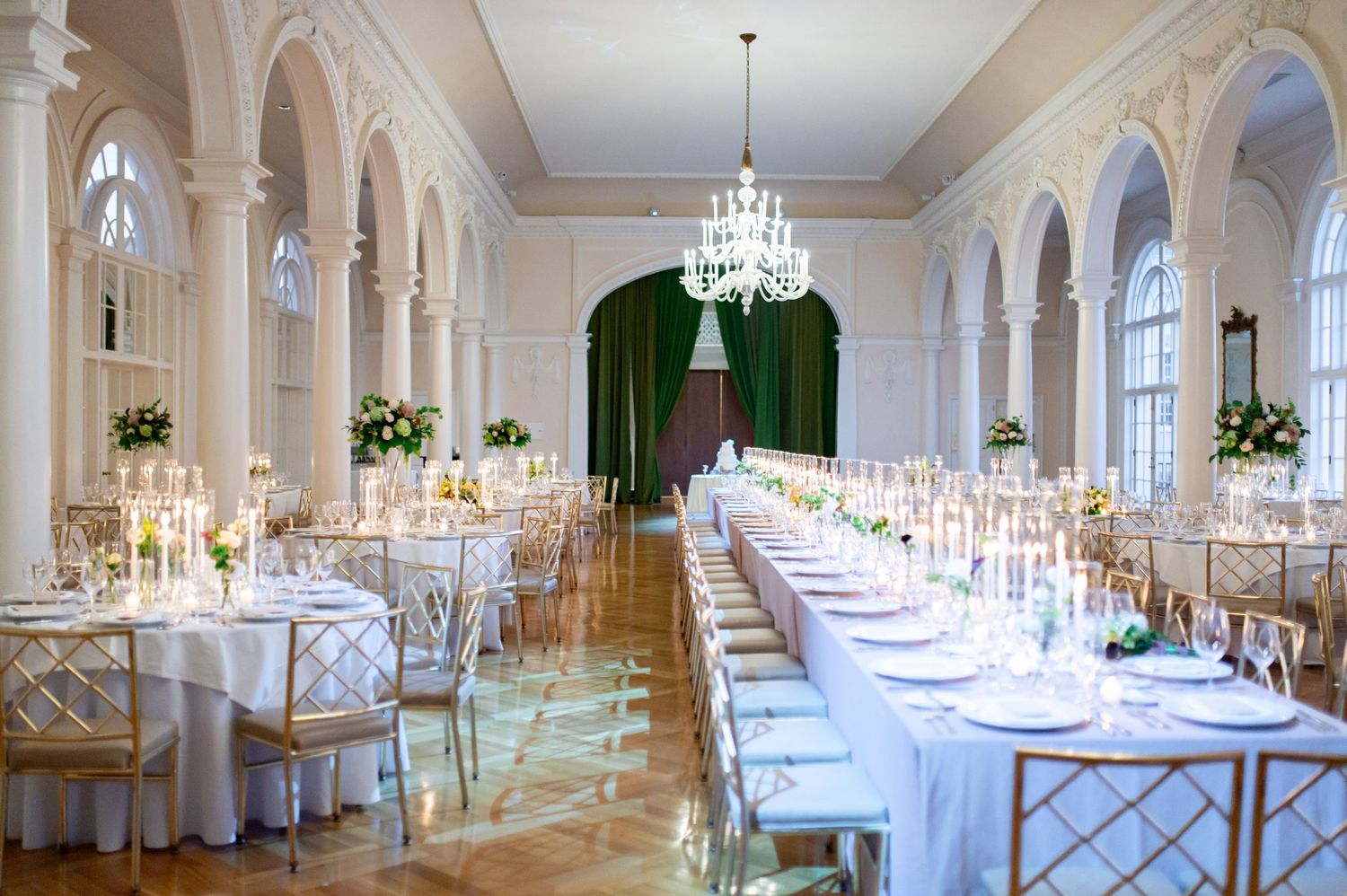 Luxurious white ballroom with arched windows and crystal chandeliers prepared for a wedding celebration.