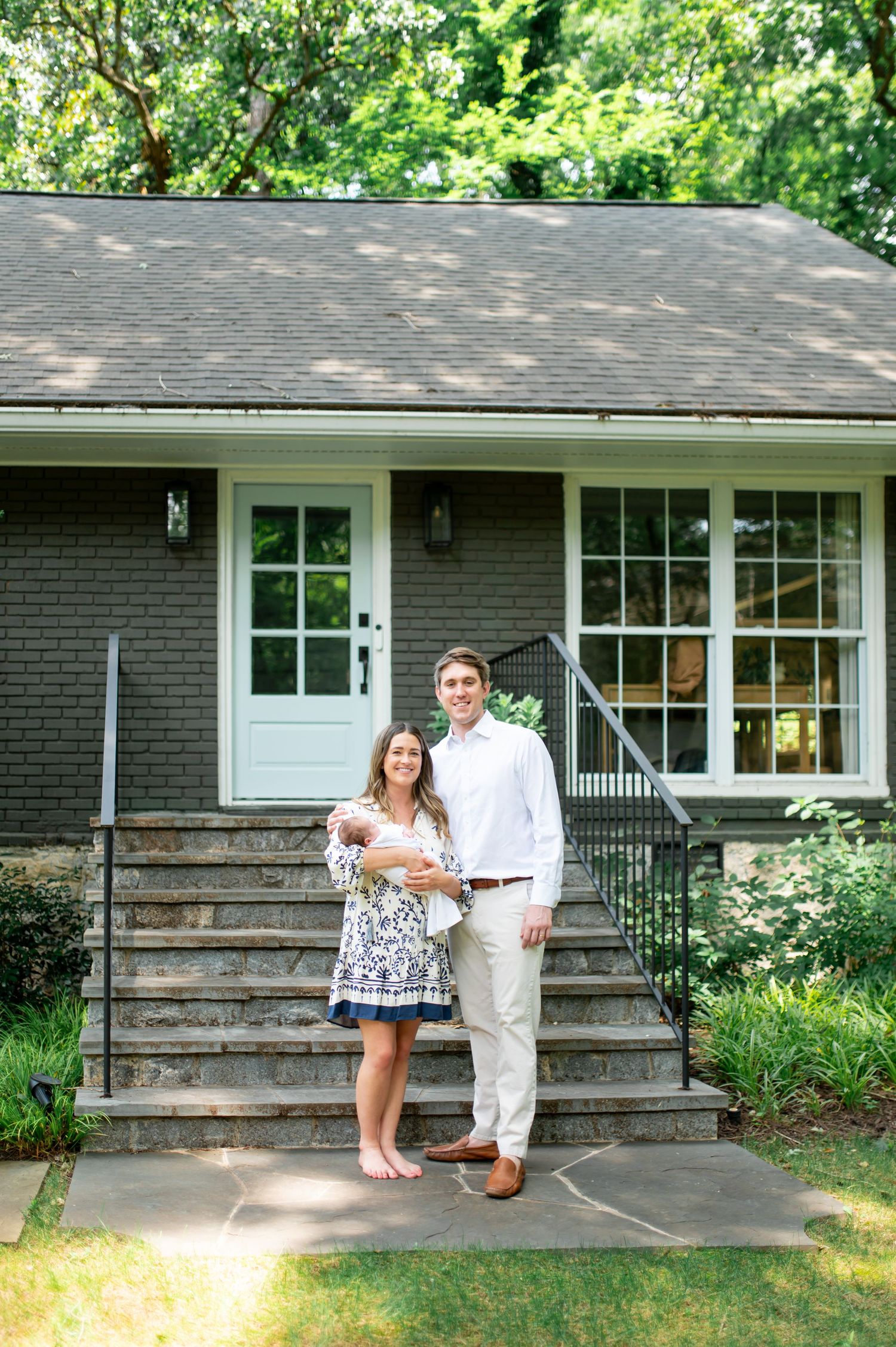 Family portrait session outside a gray brick ranch house with white trim and landscaping.