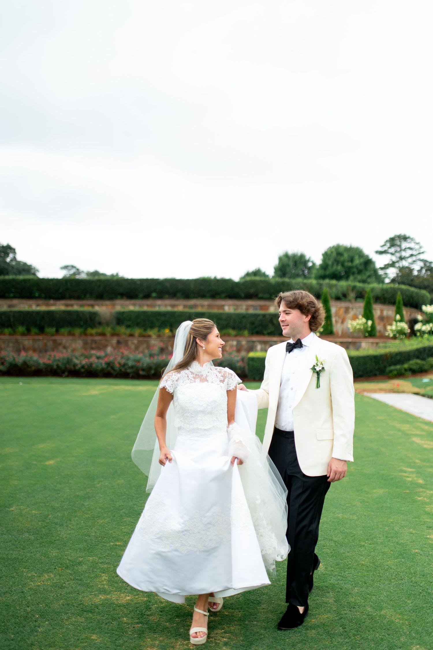 Couple walking hand in hand across a manicured lawn in wedding attire.