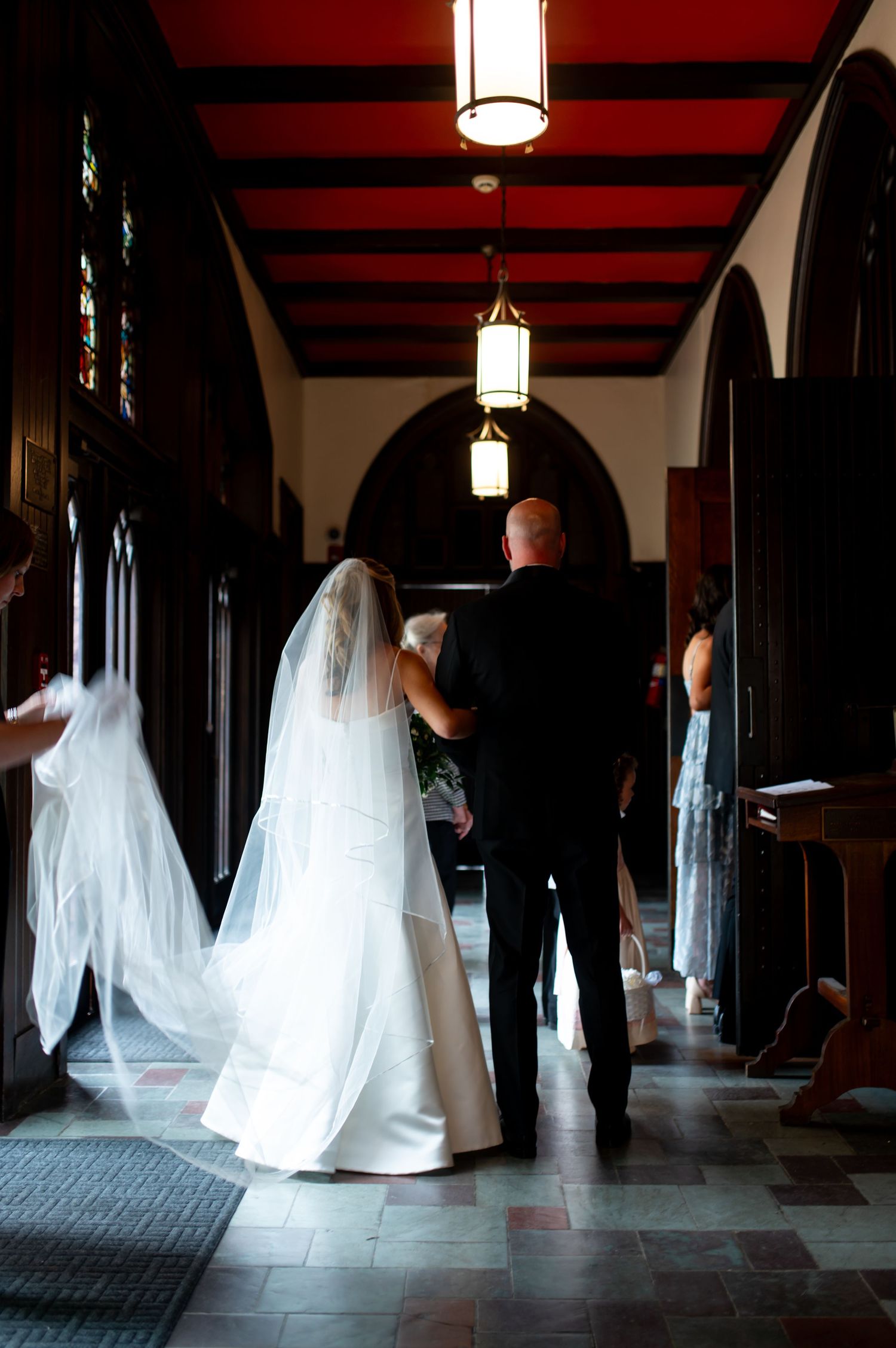 Wedding party walking through a dimly lit hallway with dramatic lighting and red ceiling beams.