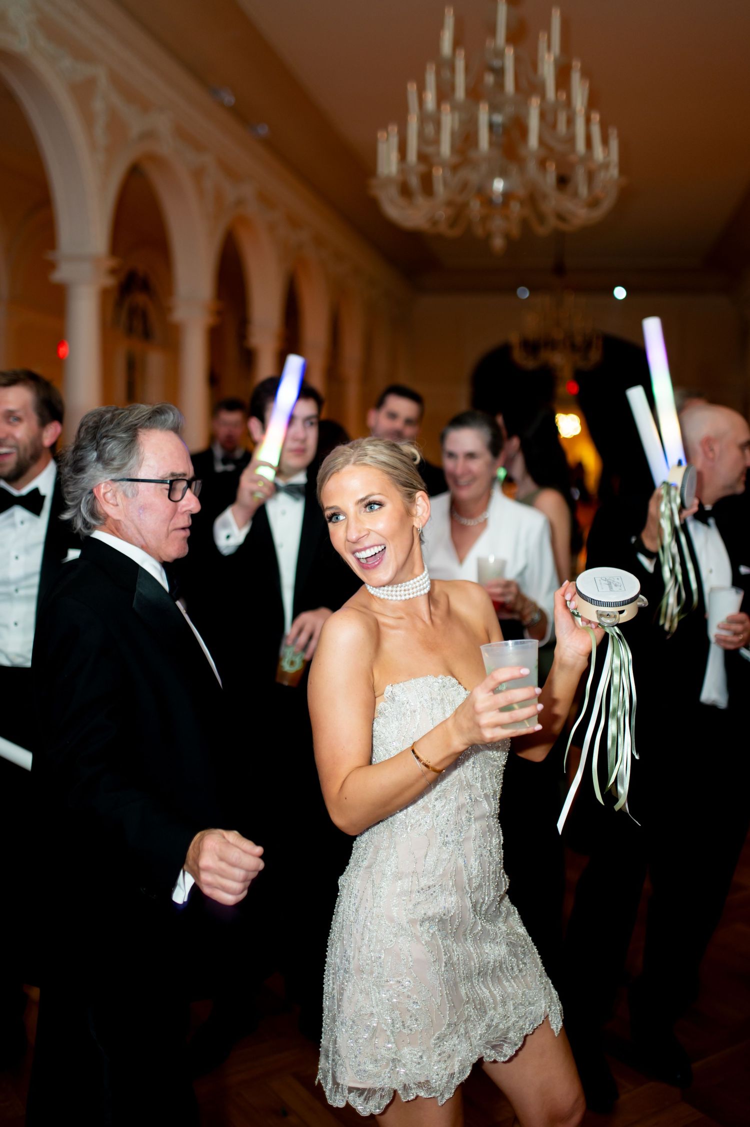 Wedding celebration in elegant ballroom with chandeliers and guests holding glow sticks.