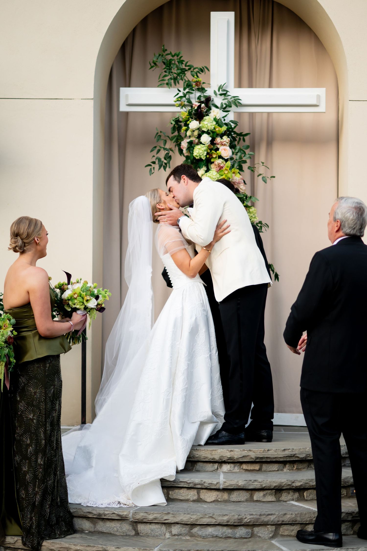 Wedding couple and guests sharing intimate moments under arched stone walkway with floral arrangements.