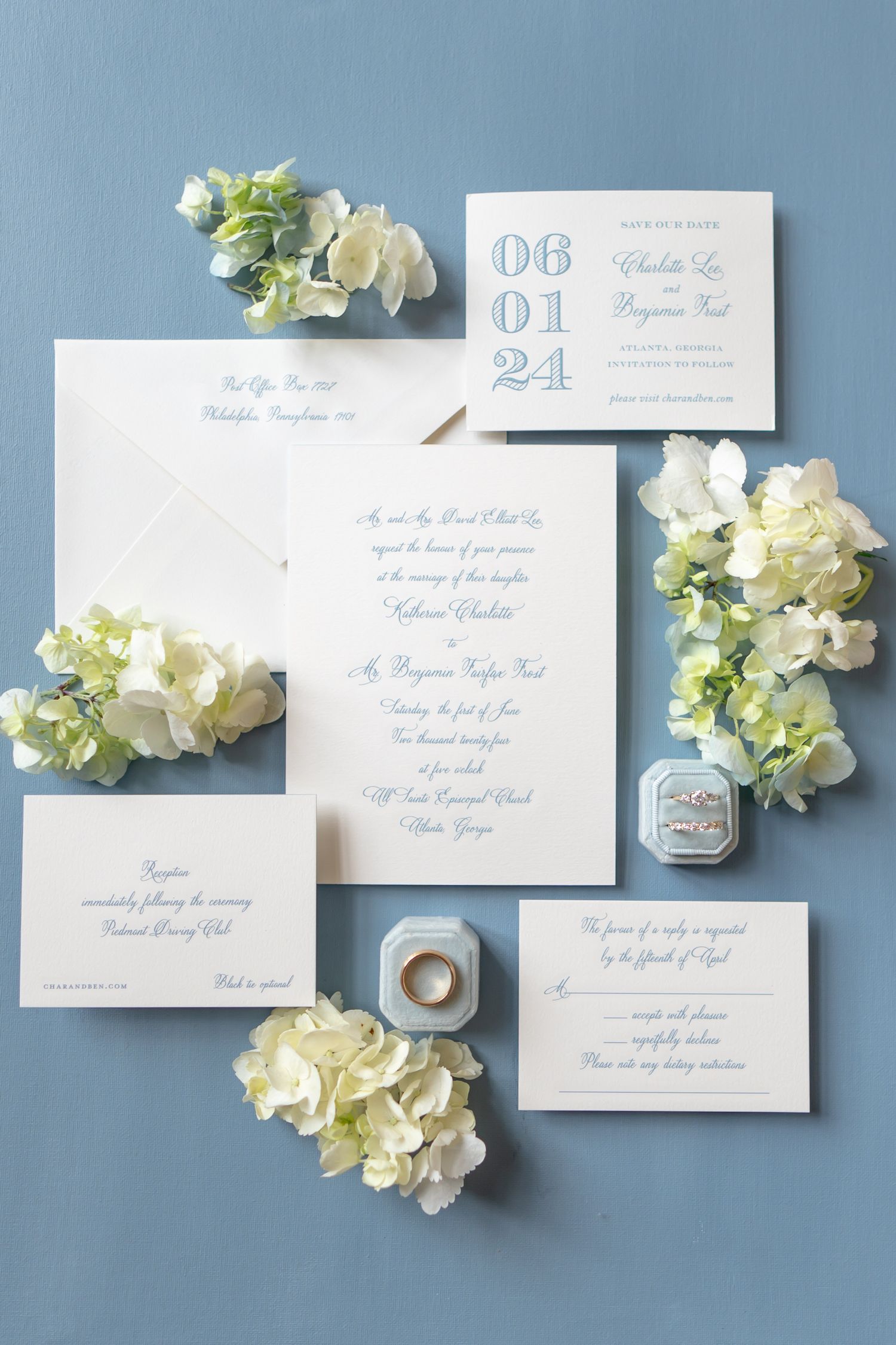 Elegant wedding invitations in light blue calligraphy with white hydrangea flowers on blue background.