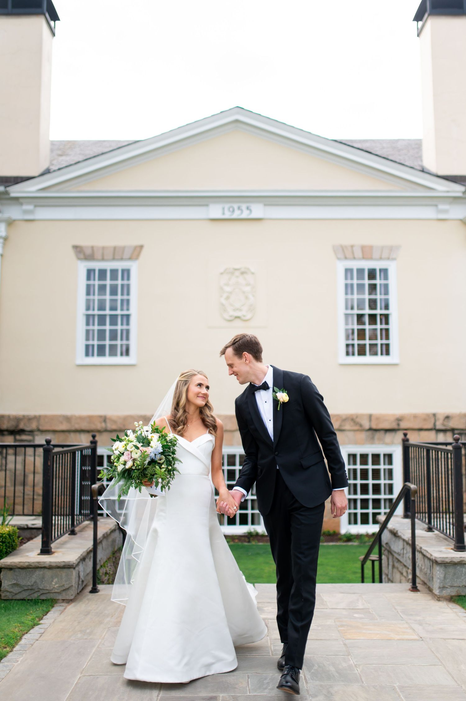 Wedding couple shares playful moments outside a classic white colonial building.
