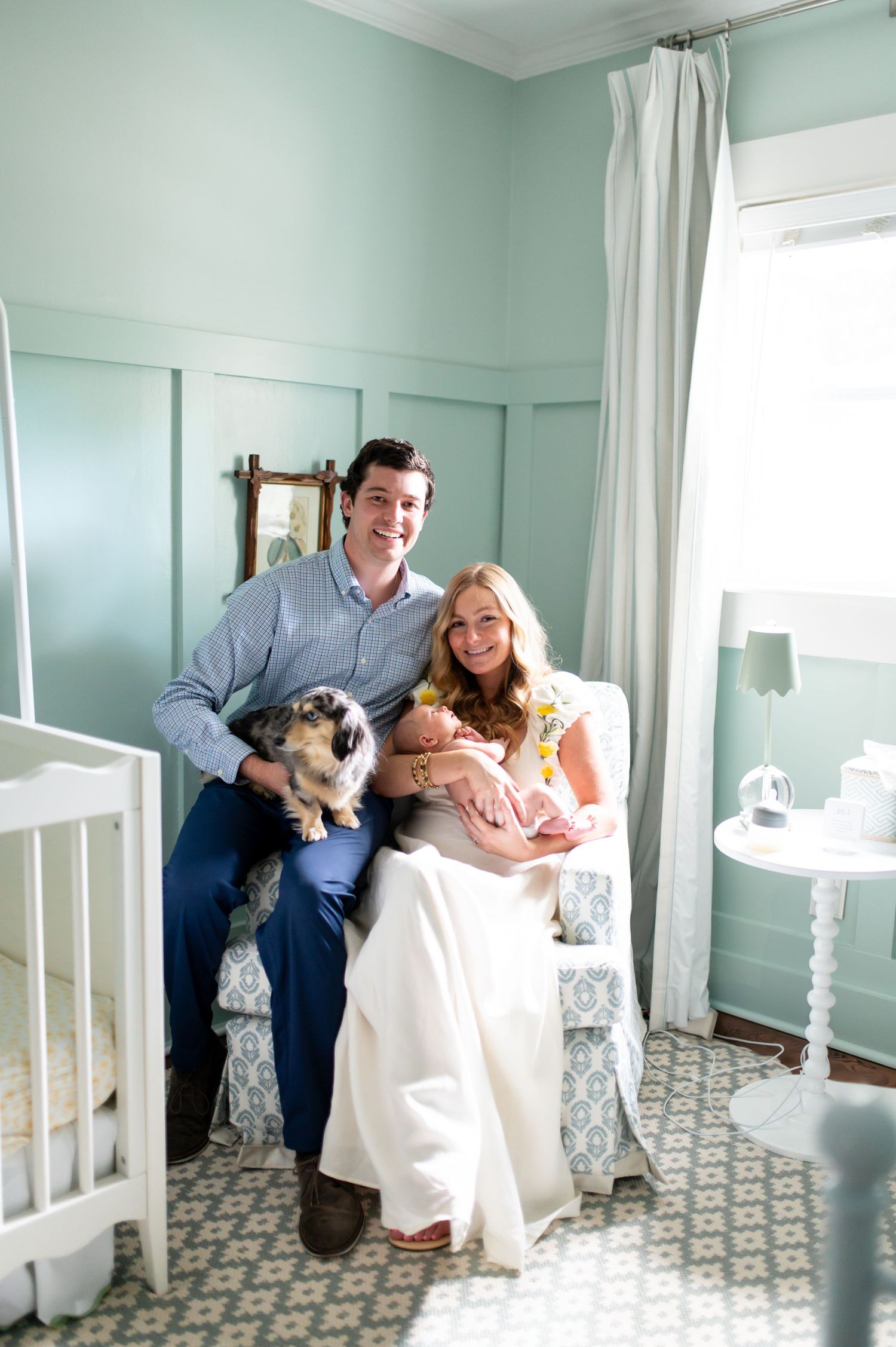 Family photos in a mint green nursery with white furniture and patterned floor.