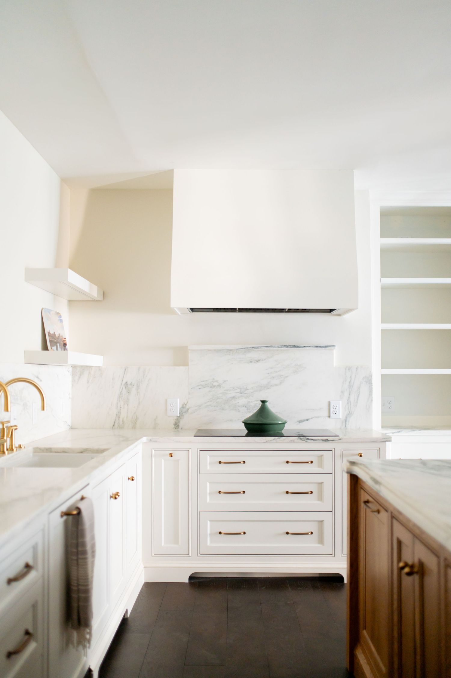 Modern white kitchen with marble backsplash, brass fixtures, and dark wood floors features clean lines and minimal design.